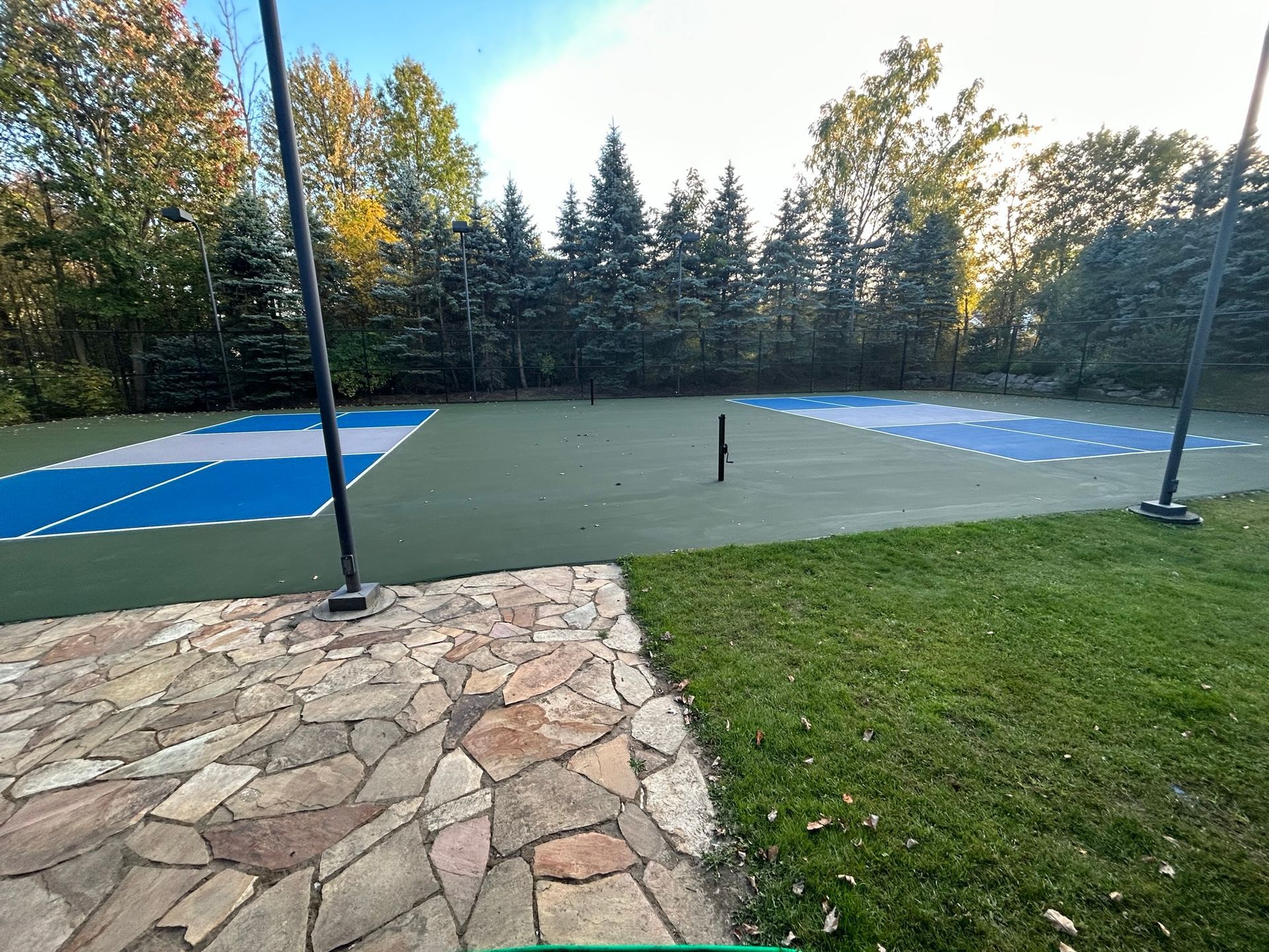 A tennis court with a stone walkway and trees in the background.