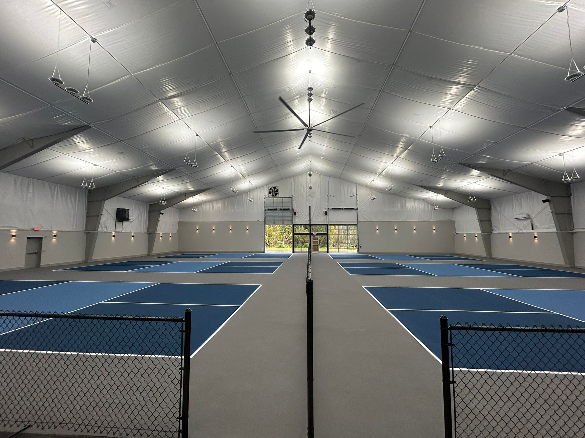 A large indoor tennis court with blue courts and a ceiling fan.