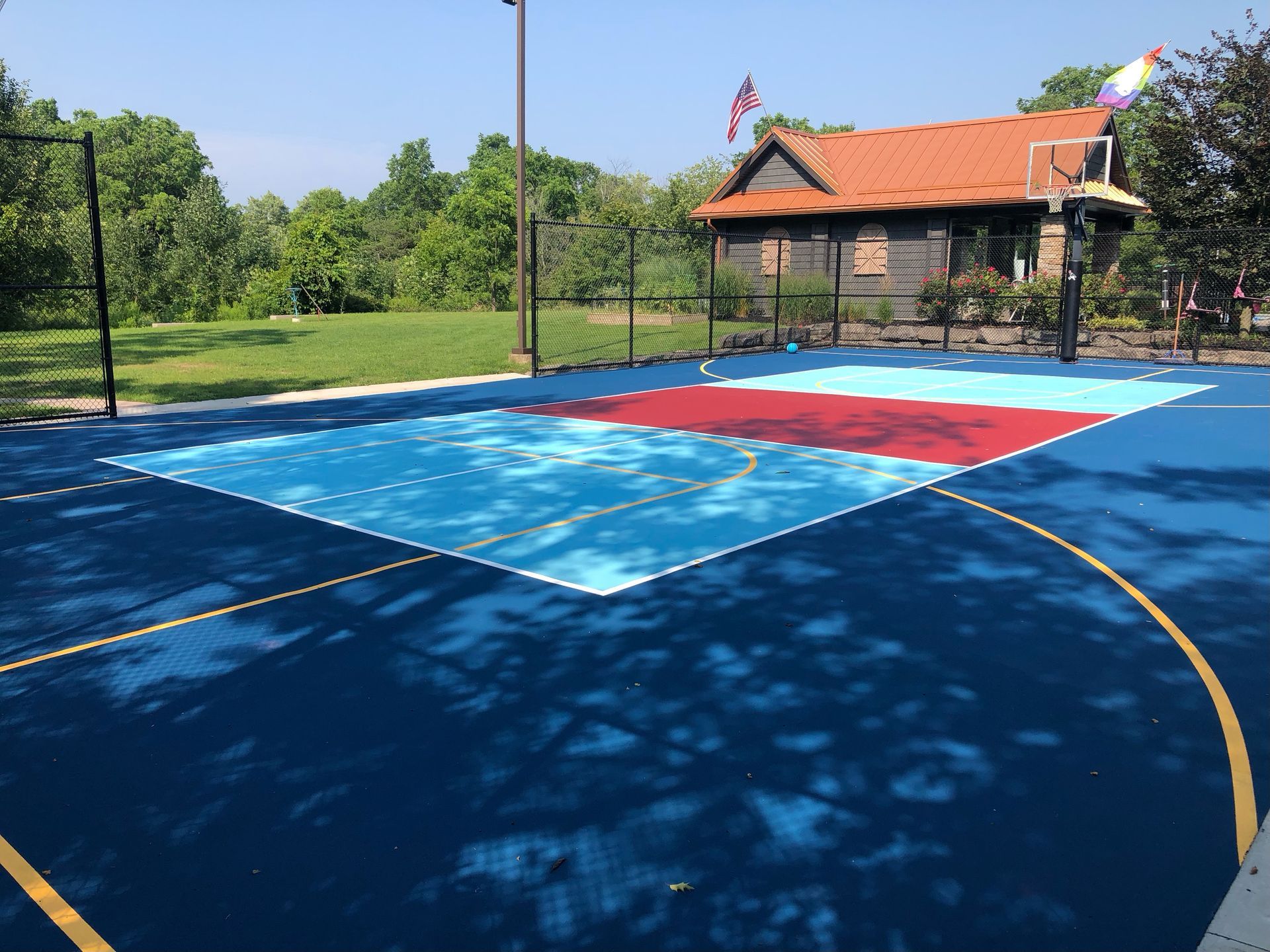 A blue and red basketball court with a house in the background