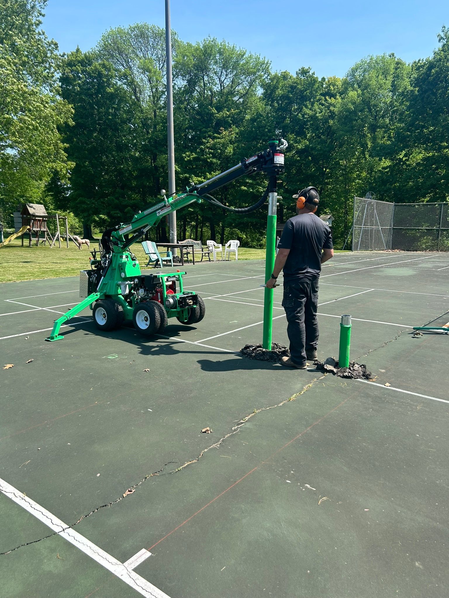 A man is standing next to a green crane on a tennis court.