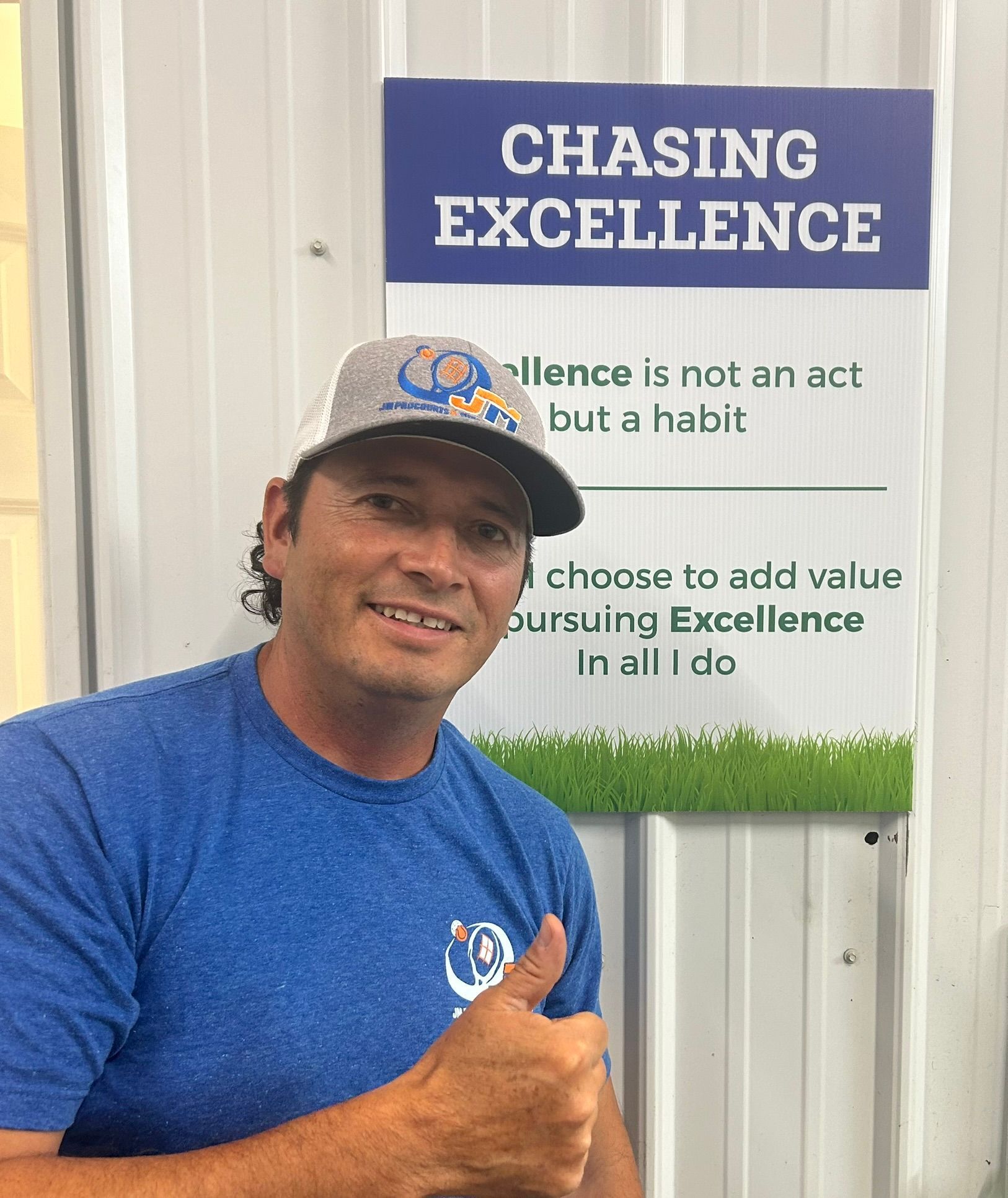 A man is giving a thumbs up in front of a sign that says chasing excellence.