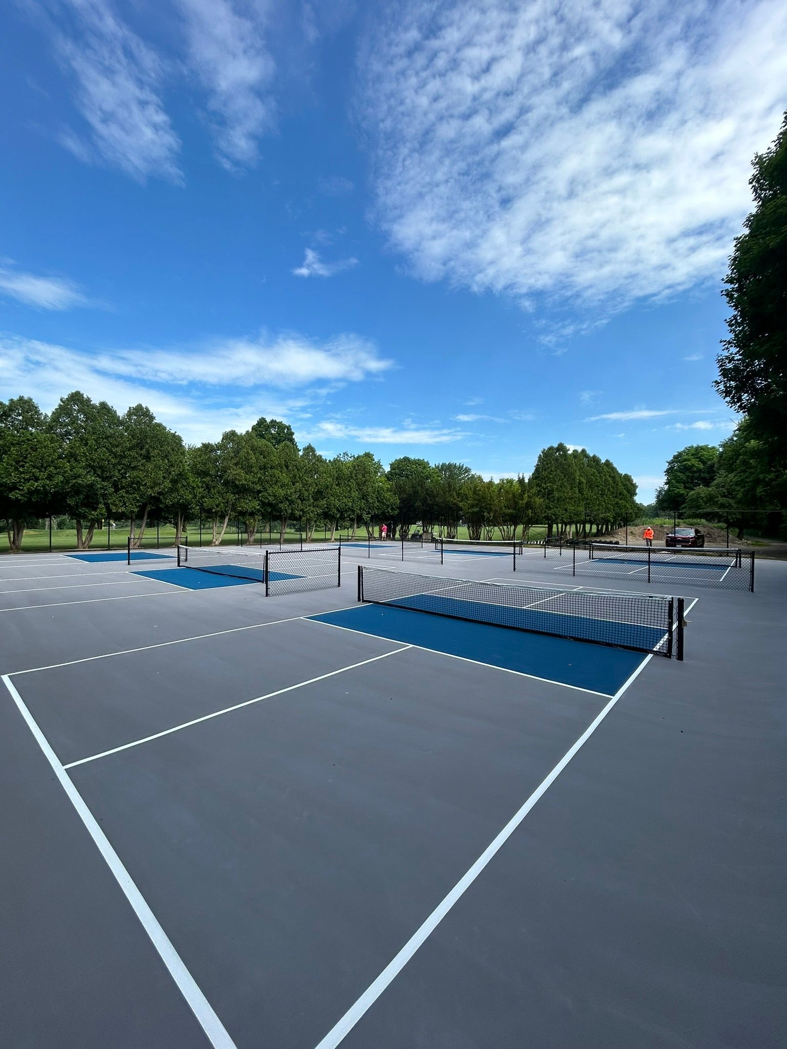A tennis court in a park on a sunny day