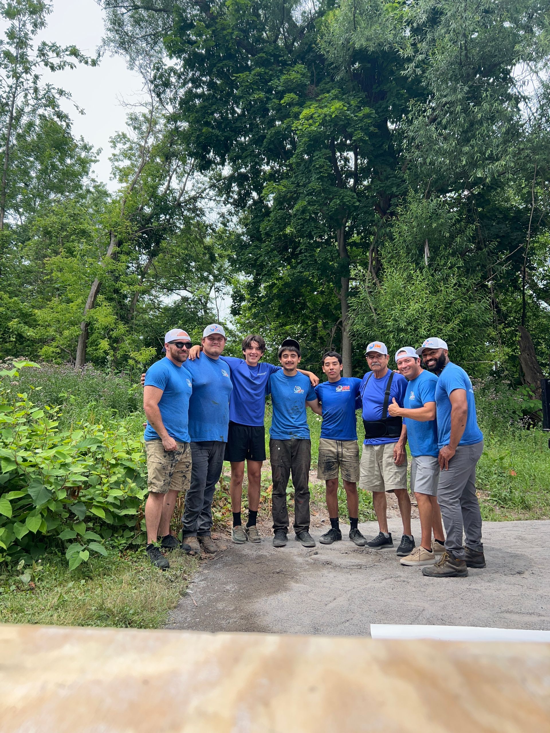 A group of men in blue shirts are posing for a picture in the woods.
