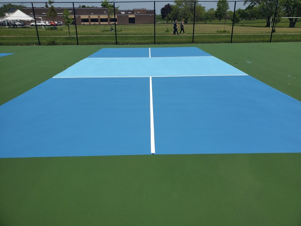 A blue and green tennis court with people walking in the background