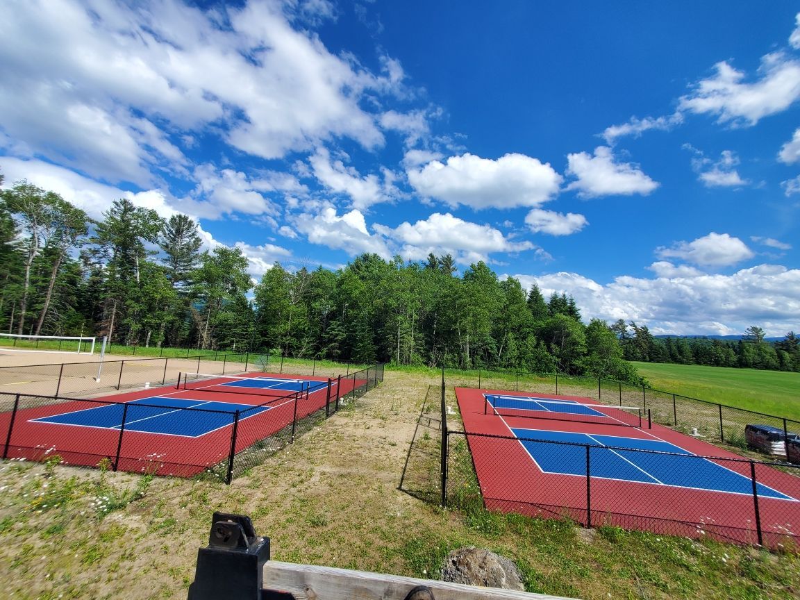 A row of tennis courts surrounded by a fence on a sunny day.