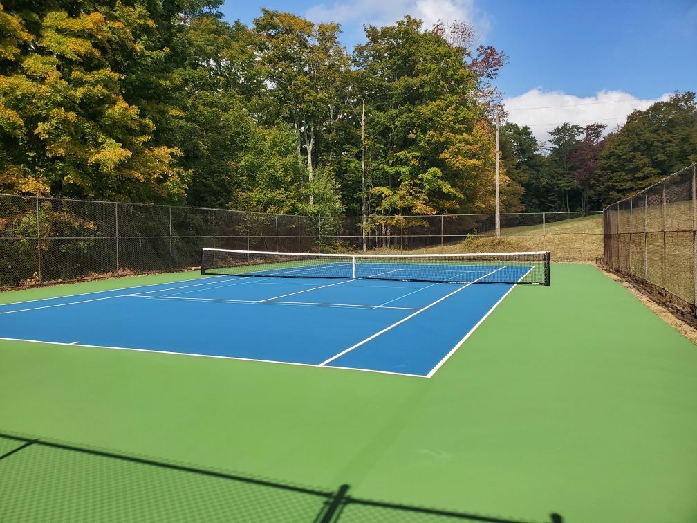 A blue and green tennis court with trees in the background
