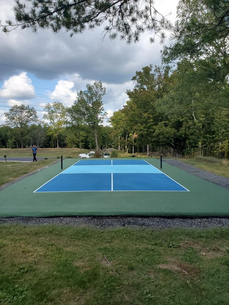 A tennis court in the middle of a field with trees in the background.