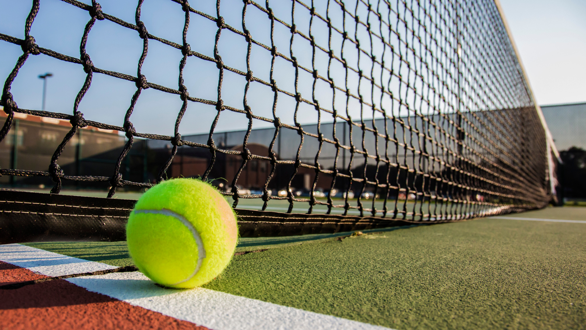 A tennis ball is sitting on the line of a tennis court.