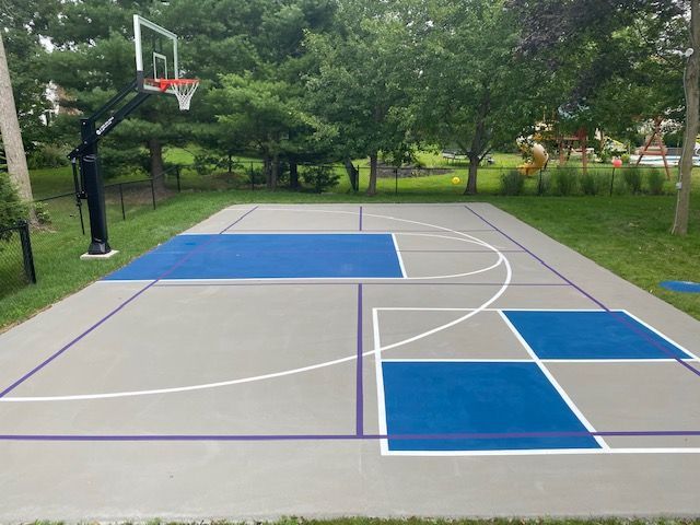 A basketball court in a backyard with a basketball hoop surrounded by trees.