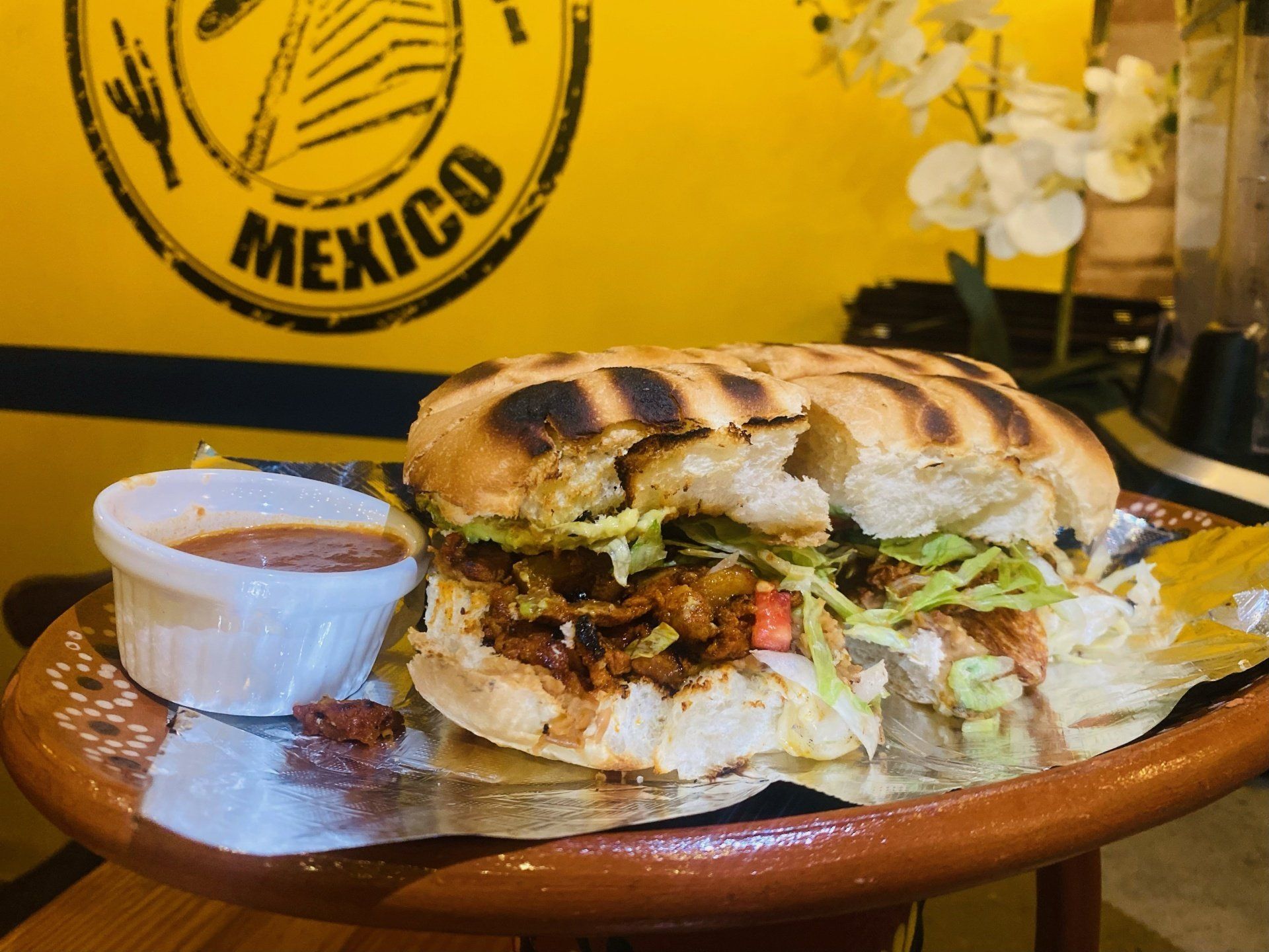 A sandwich is sitting on a table next to a small bowl of sauce.