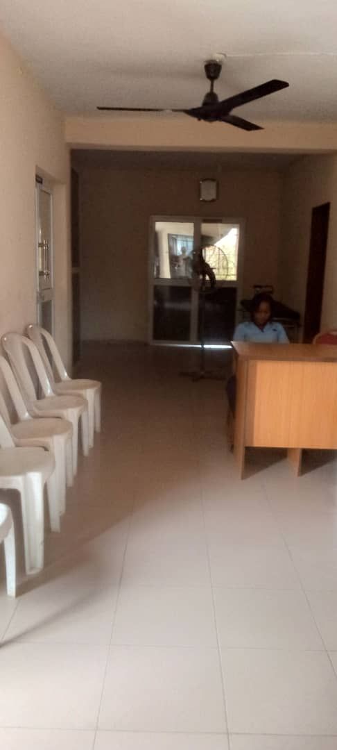 A man is sitting at a desk in a room with chairs and a ceiling fan.