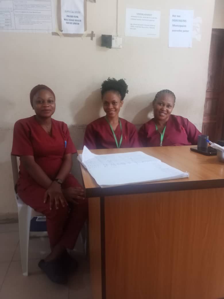 Three nurses are posing for a picture while sitting at a desk.