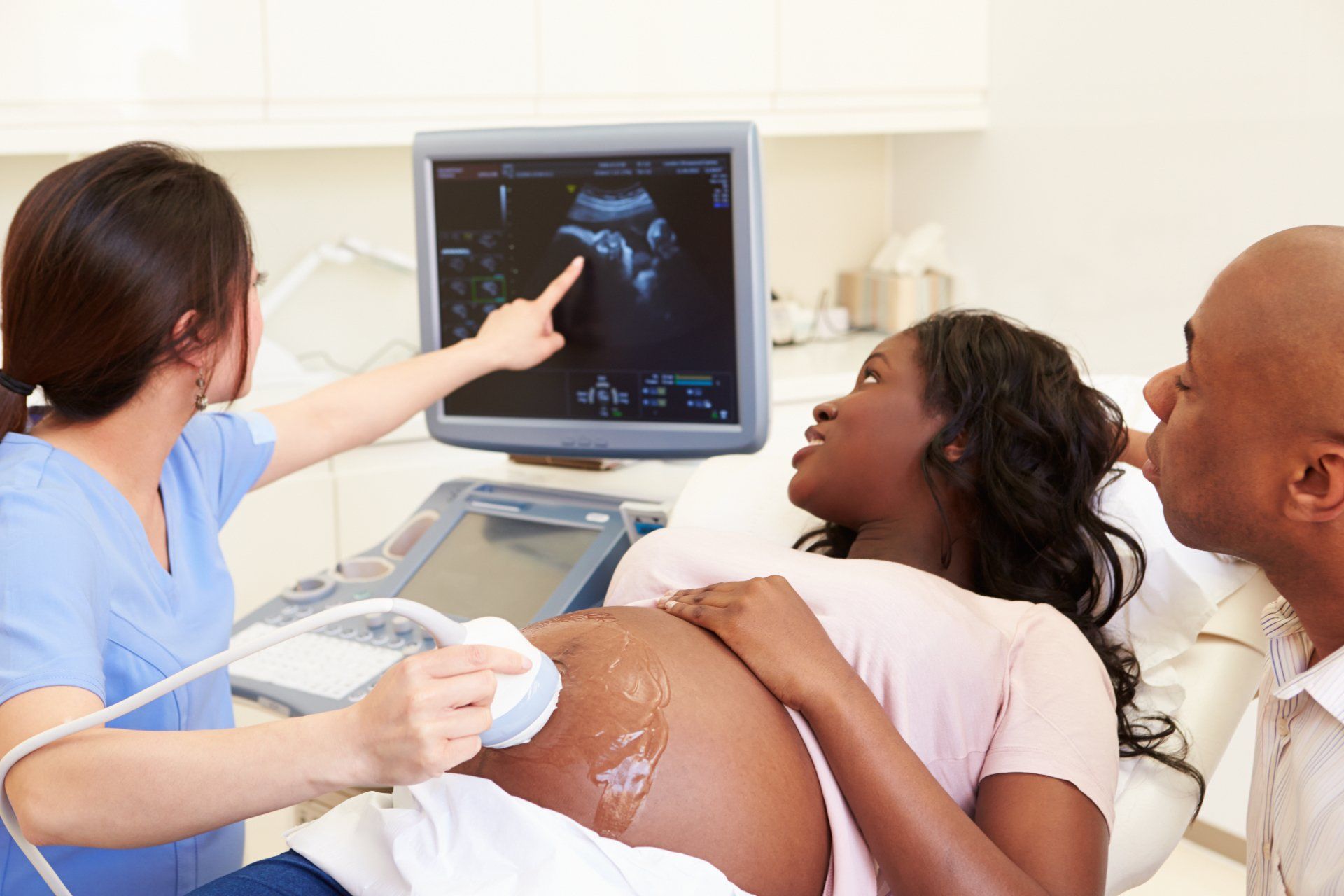 A pregnant woman is getting an ultrasound from a doctor while a man watches.