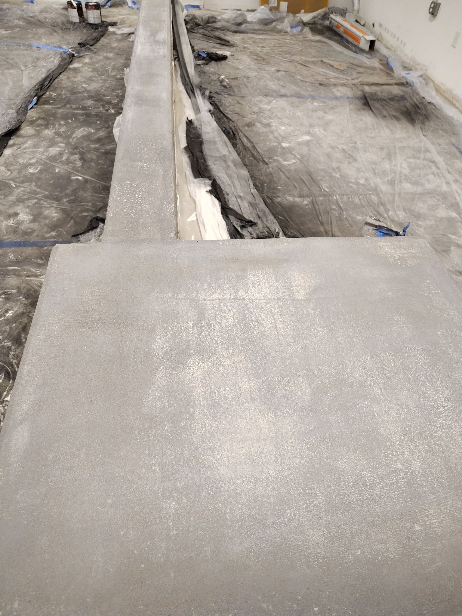 Concrete floor being prepared for construction, with trenches and rectangular platform. Gray and dark colors.