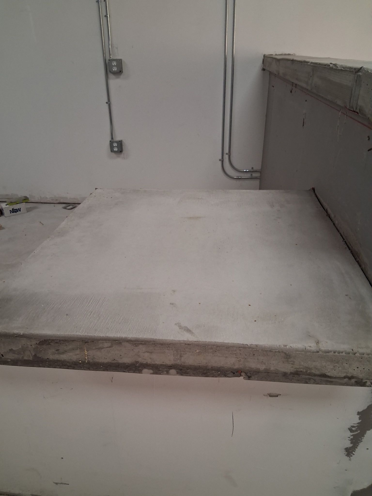 Concrete platform against a white wall. Conduit and electrical boxes are visible.