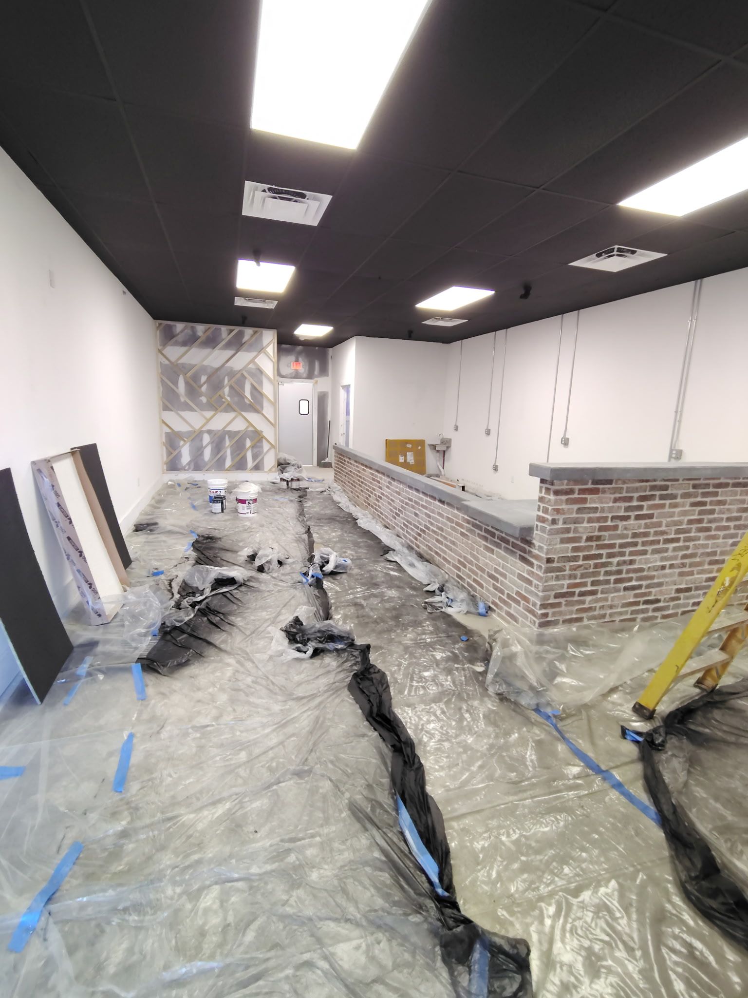 Interior construction site with black ceiling, white walls, and plastic covering the floor.