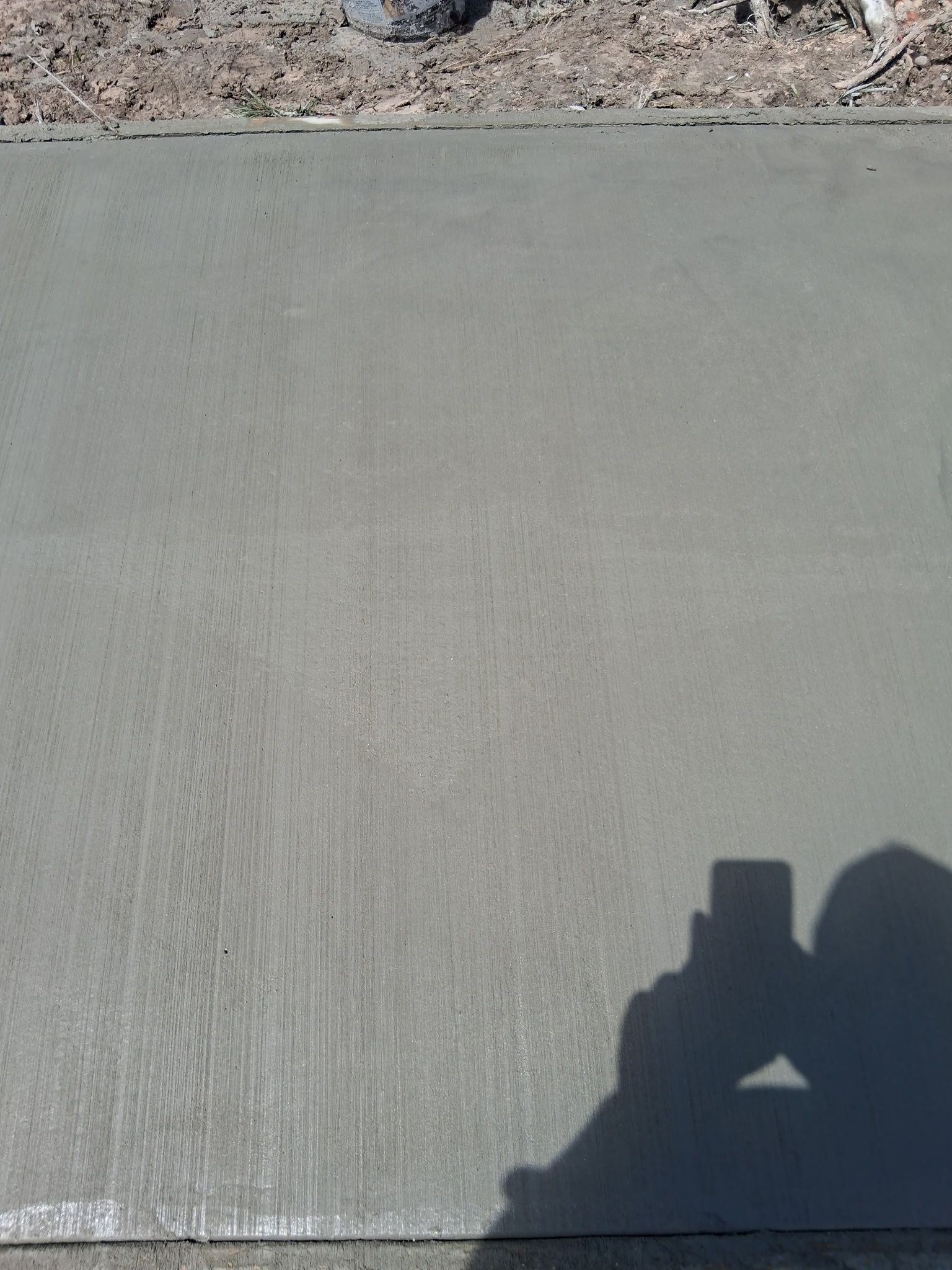 Newly poured concrete sidewalk, slightly textured, with a person's shadow in the lower right corner.