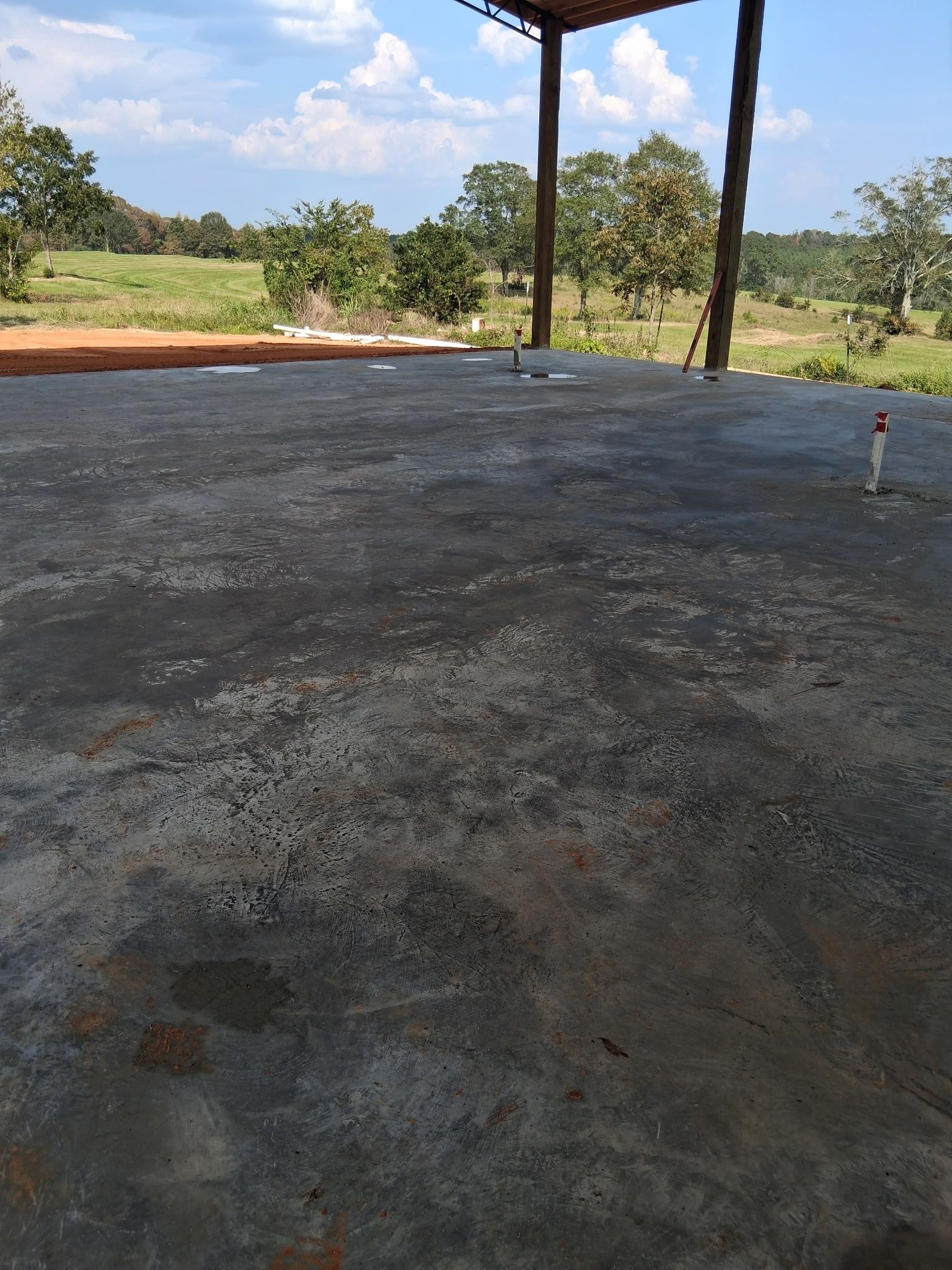Concrete floor under a metal roof, in a rural setting with trees and a green field visible in the background.