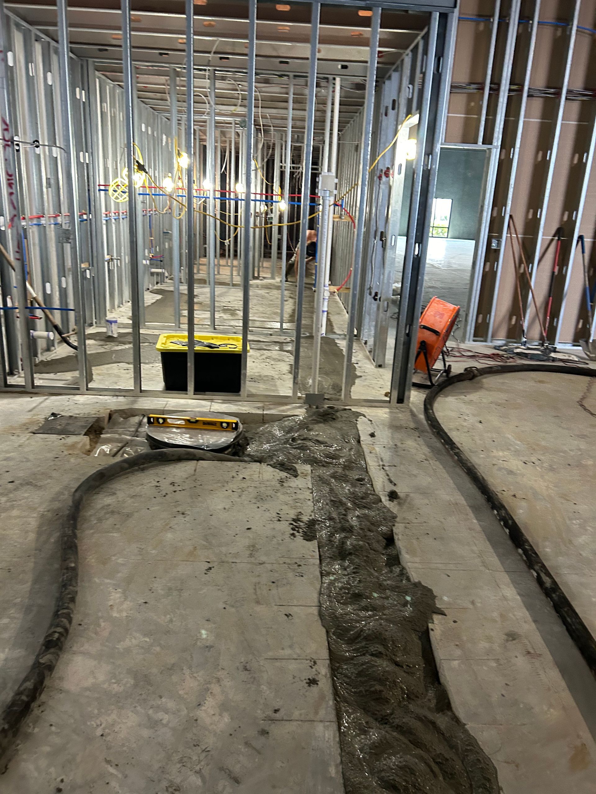 Construction site: metal studs, concrete floor, wet cement, black conduit, yellow toolbox.