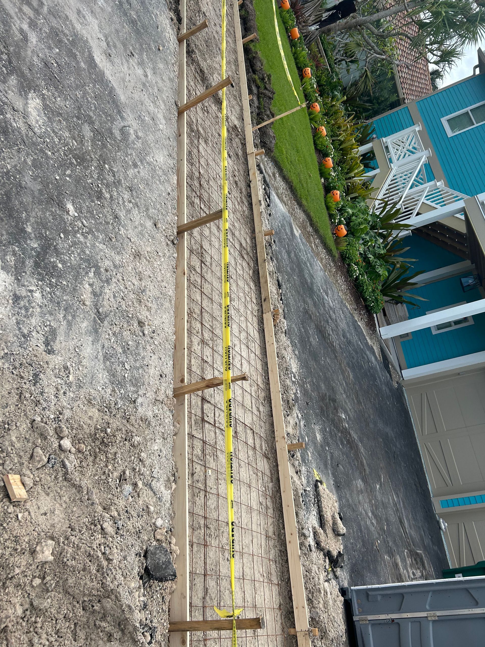 Construction site: wooden forms on ground for concrete work, next to a grassy lawn and building.