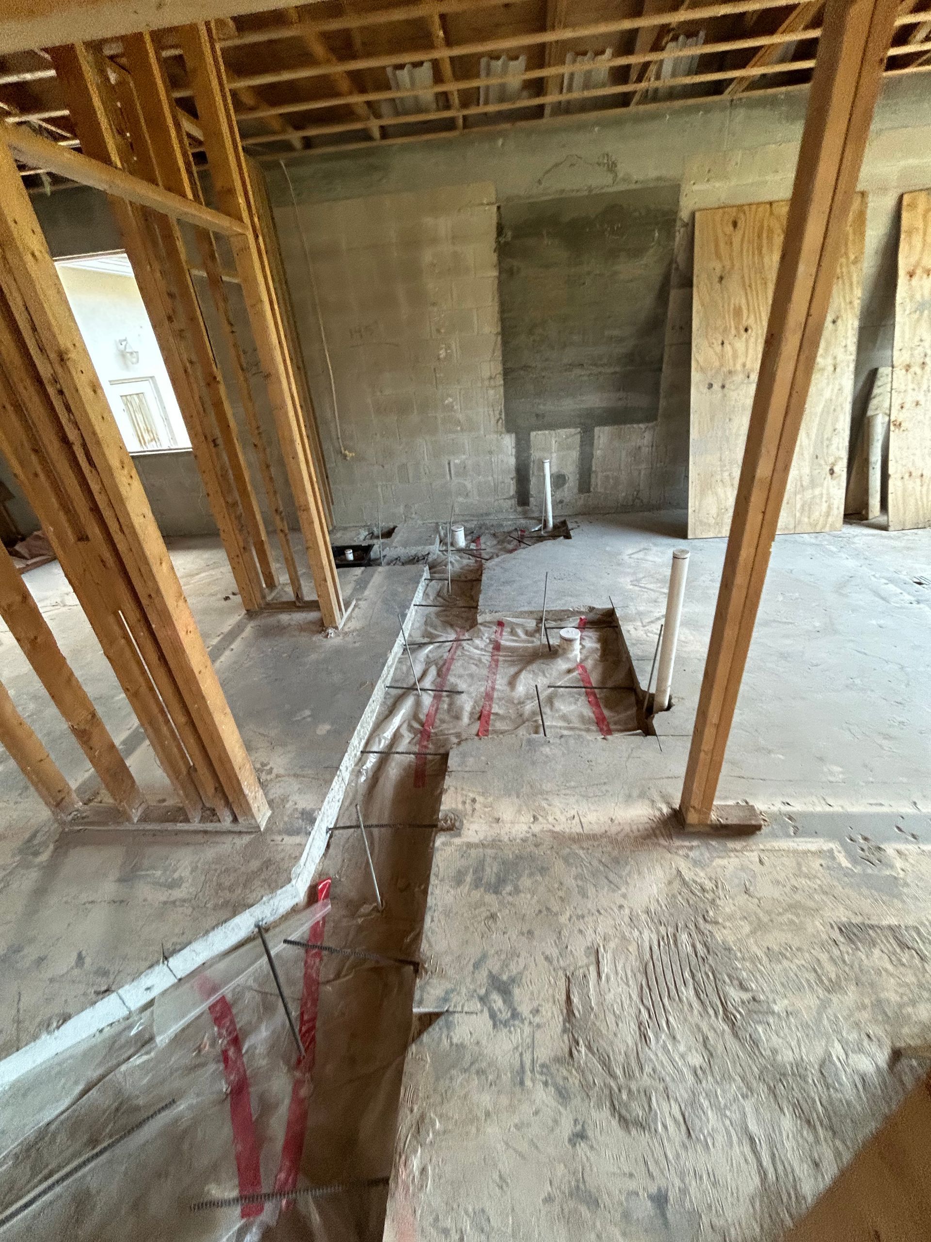 Interior construction site with wooden framing, exposed concrete, and plumbing.
