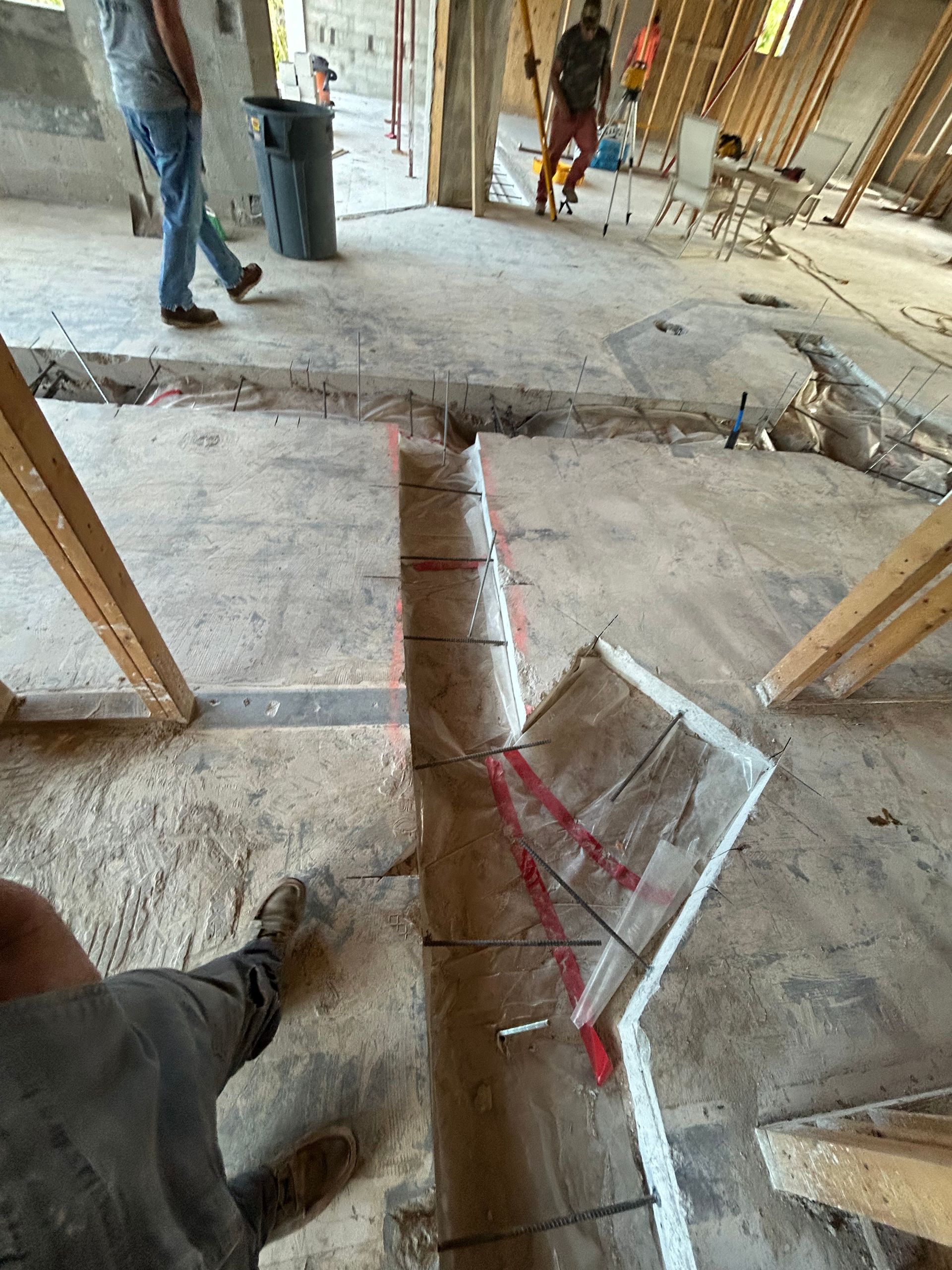 Construction site with concrete floor cut for a trench, marked with red lines. Two workers are present.