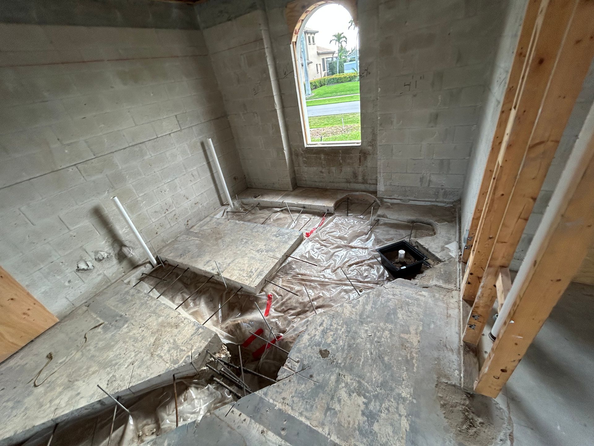 Interior of unfinished room with concrete block walls, window, and damaged concrete floor.