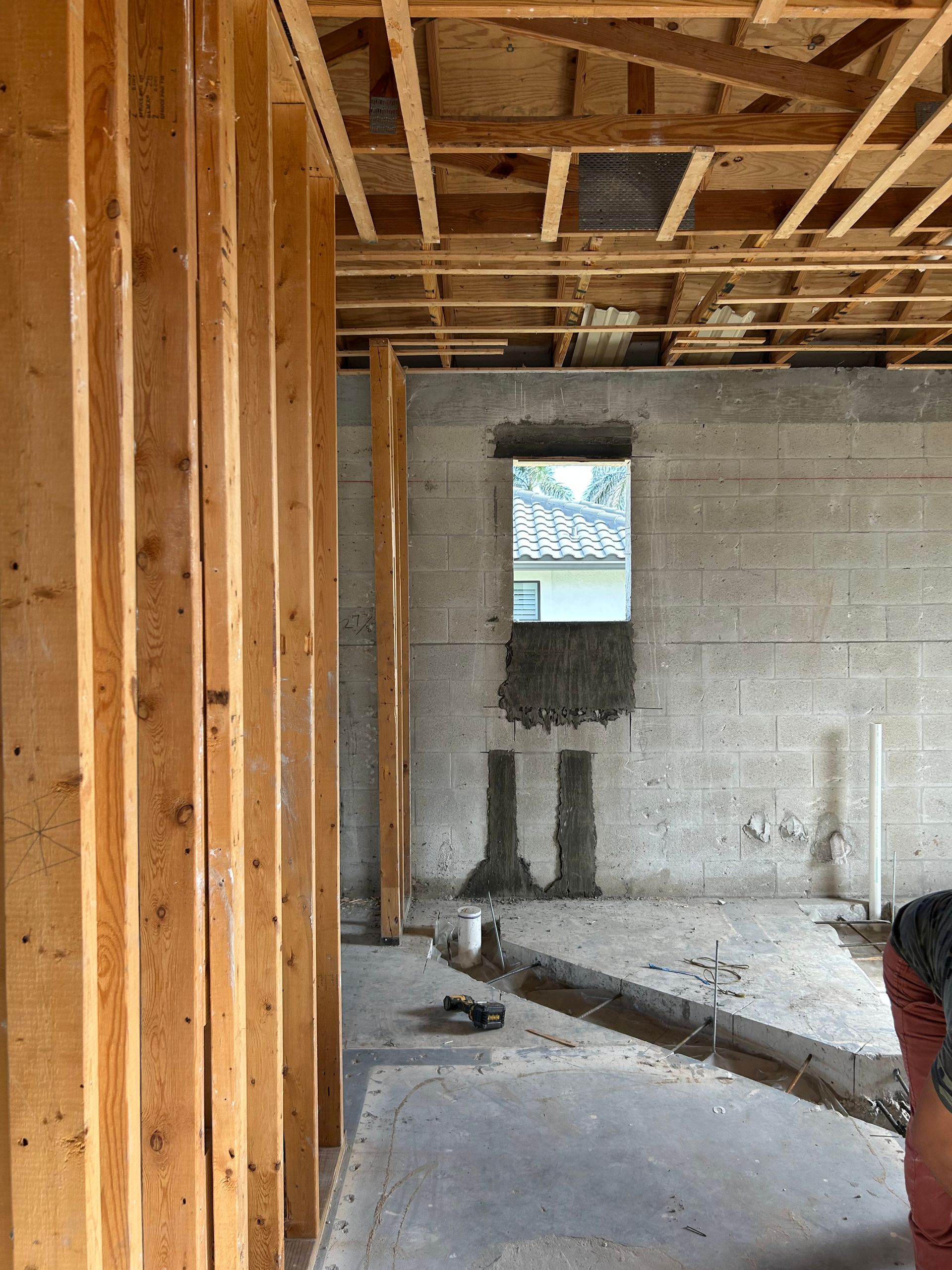 Interior framing of a building under construction, showing wooden studs, concrete walls, and a window.