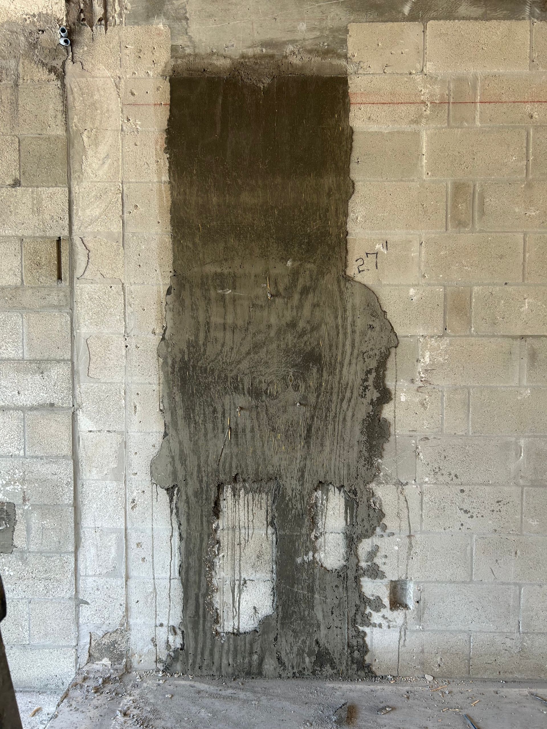 Concrete block wall with a rectangular patch of wet concrete.