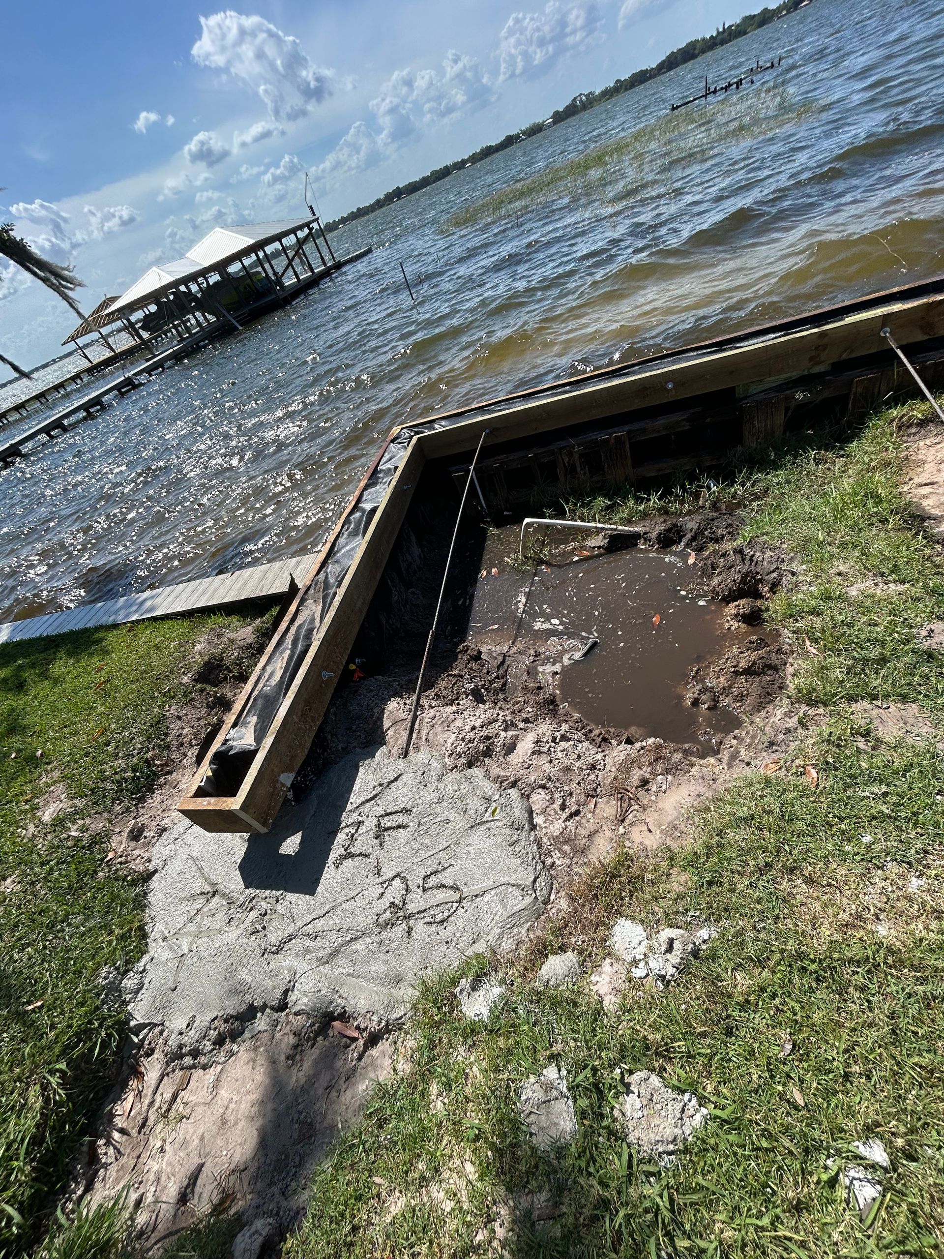 Wooden dock on a lake with eroded shoreline and muddy area.