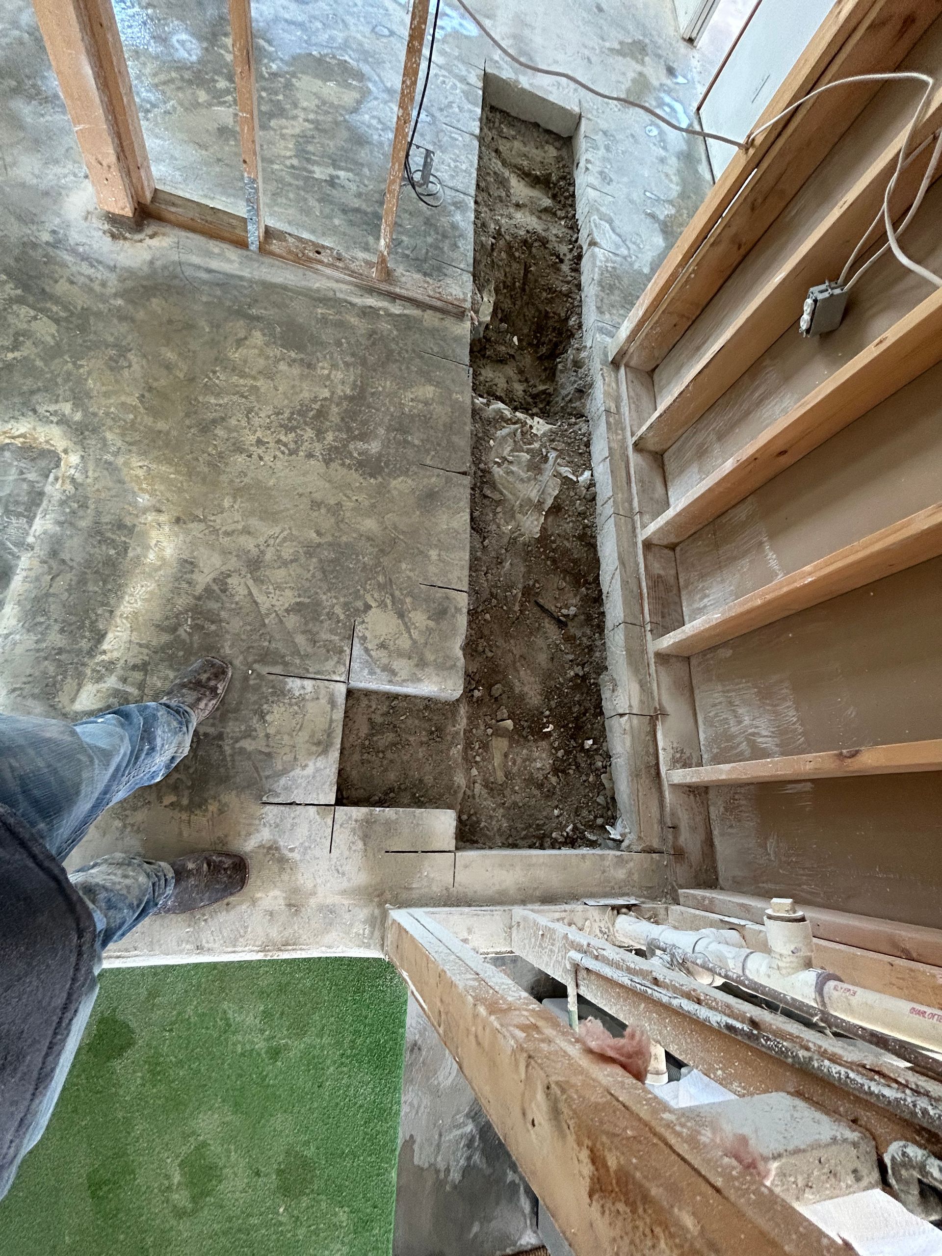 Concrete floor with a trench cut into it, near wood framing.