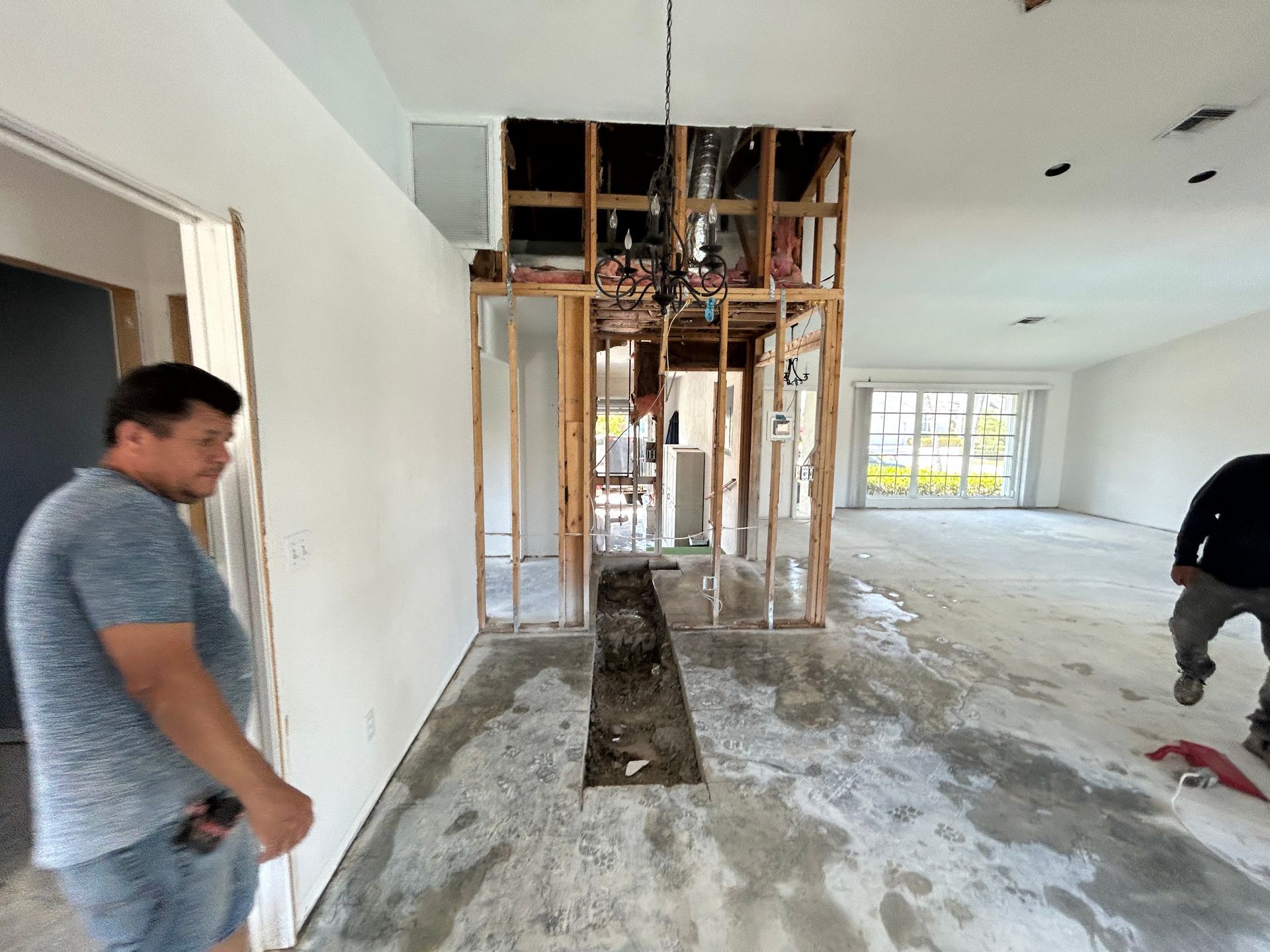 Men in a room under renovation. Interior wall studs exposed, concrete floor, white walls, and a chandelier.