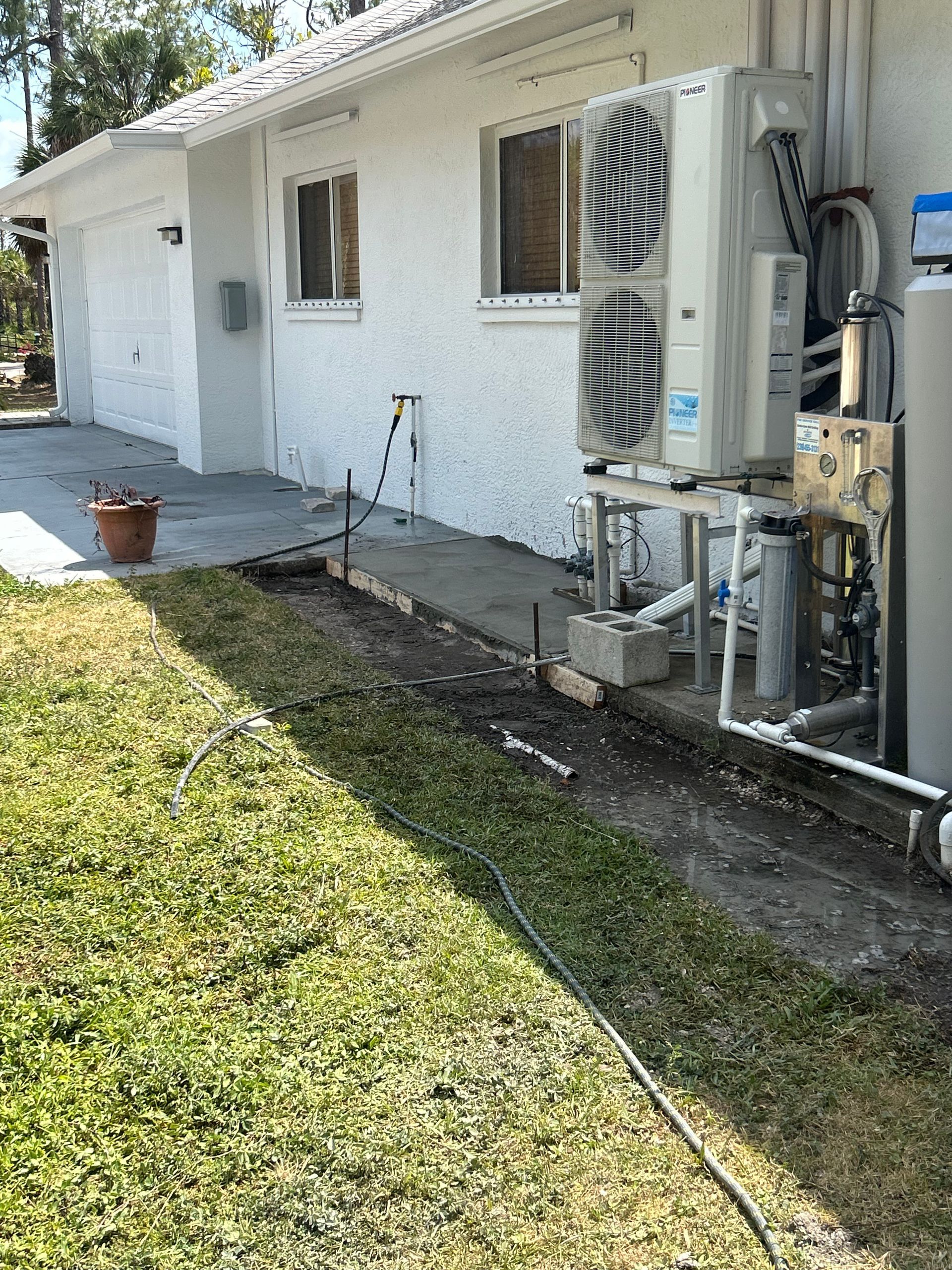 Exterior view of a white stucco house with an air conditioning unit and water heater, on a grassy lawn.