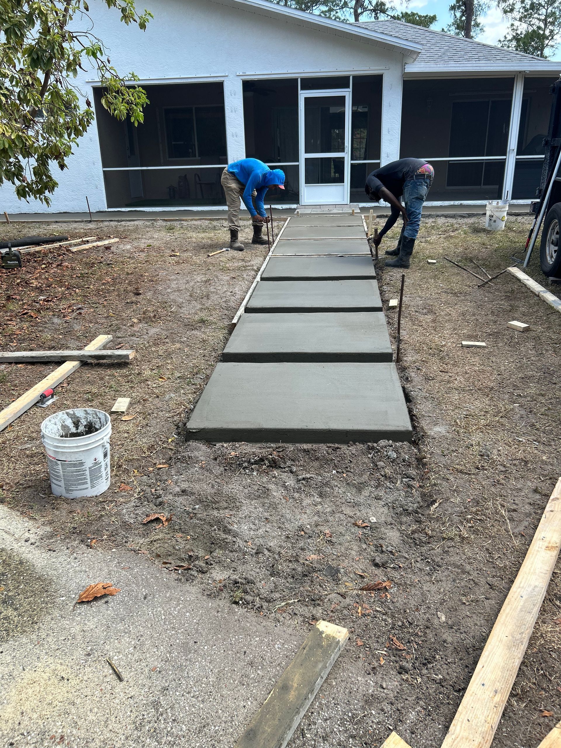 Two workers laying concrete pavers on a pathway leading to a house.