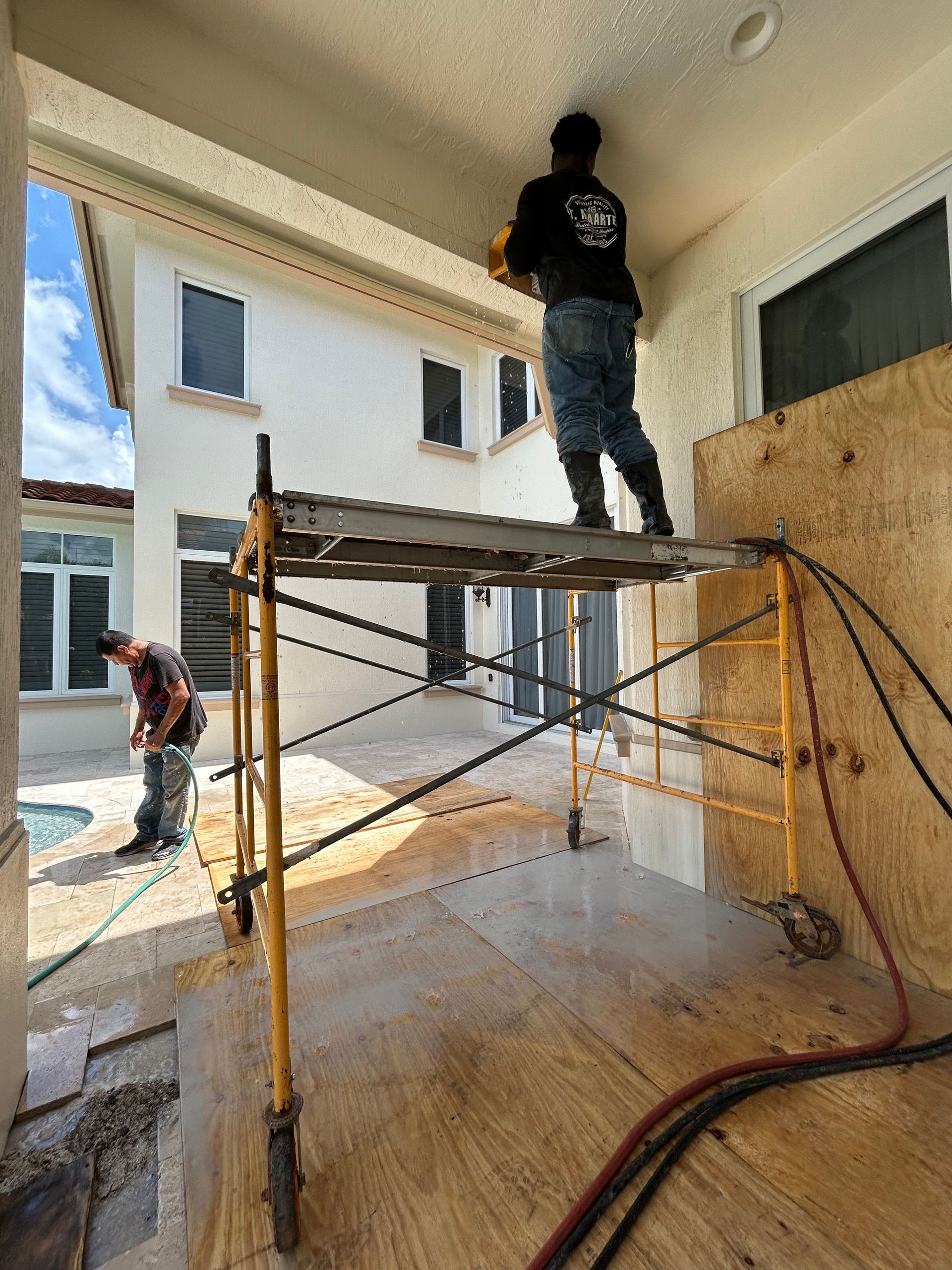 Two workers repairing a white outdoor structure. One stands on a scaffold, the other works below.
