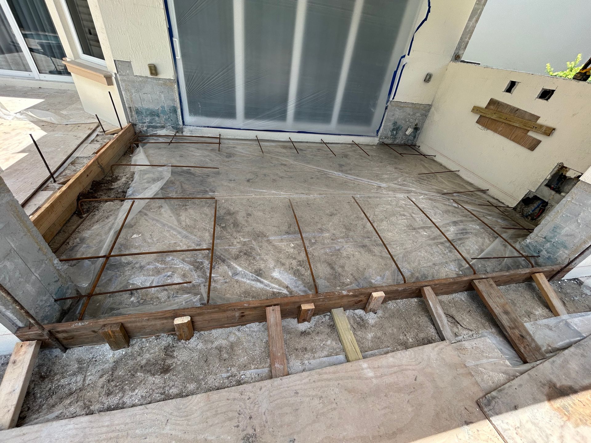 Construction site: wooden forms, rebar grid on a concrete base, awaiting concrete for a patio.