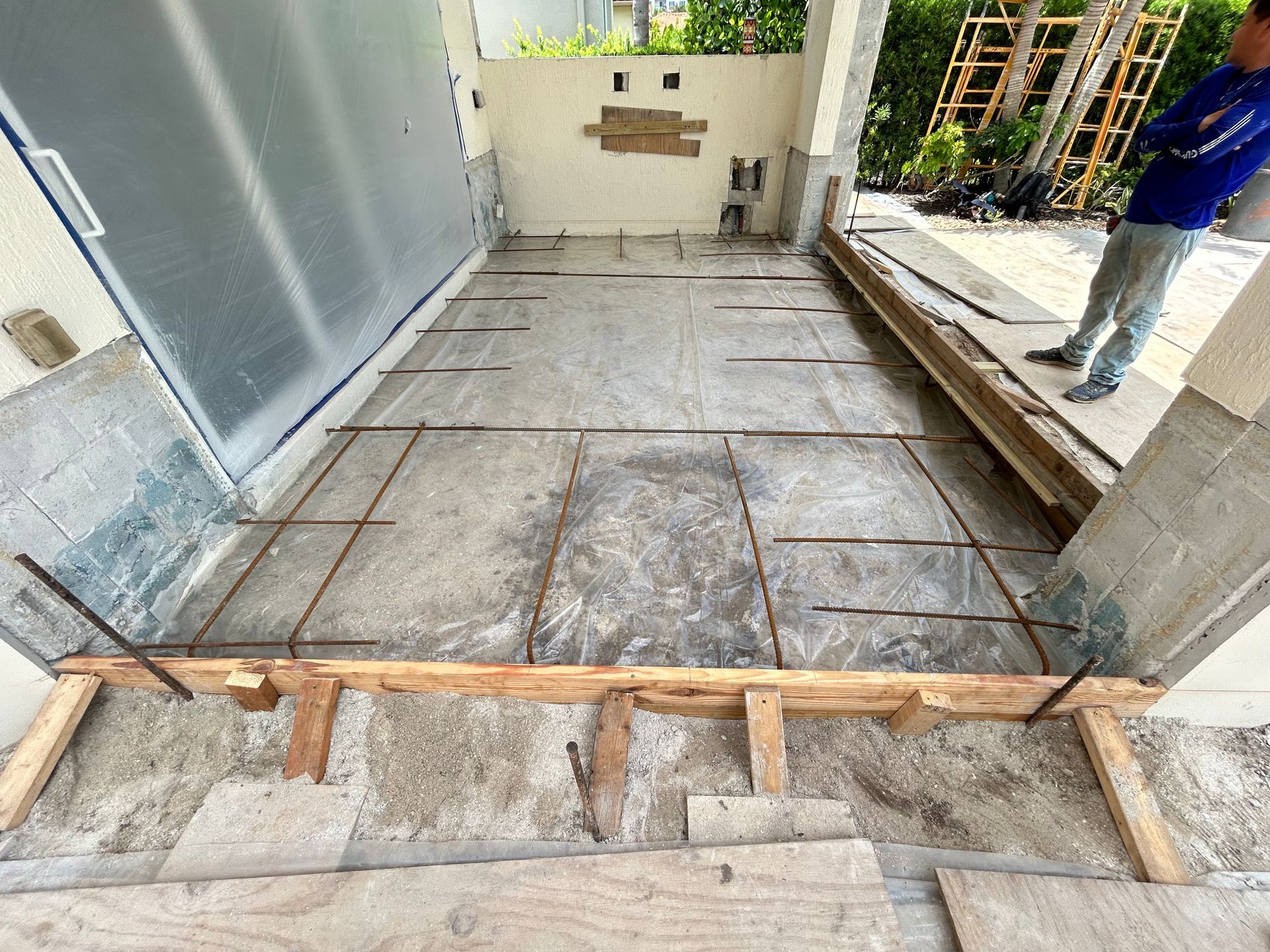Concrete slab under construction with rebar framework, wooden supports, and a person standing nearby.