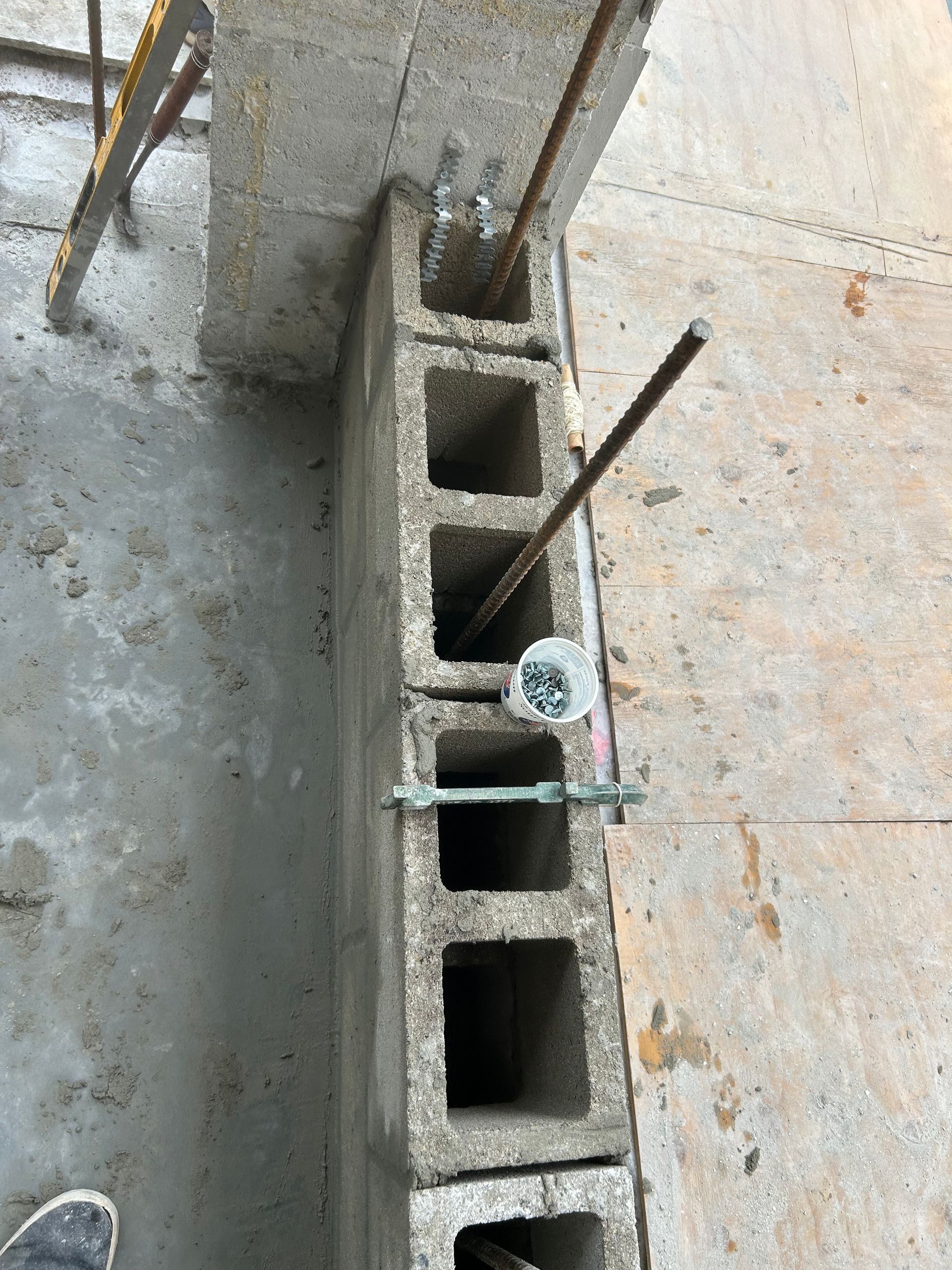 Concrete block wall with rebar extending through it, under a concrete structure.