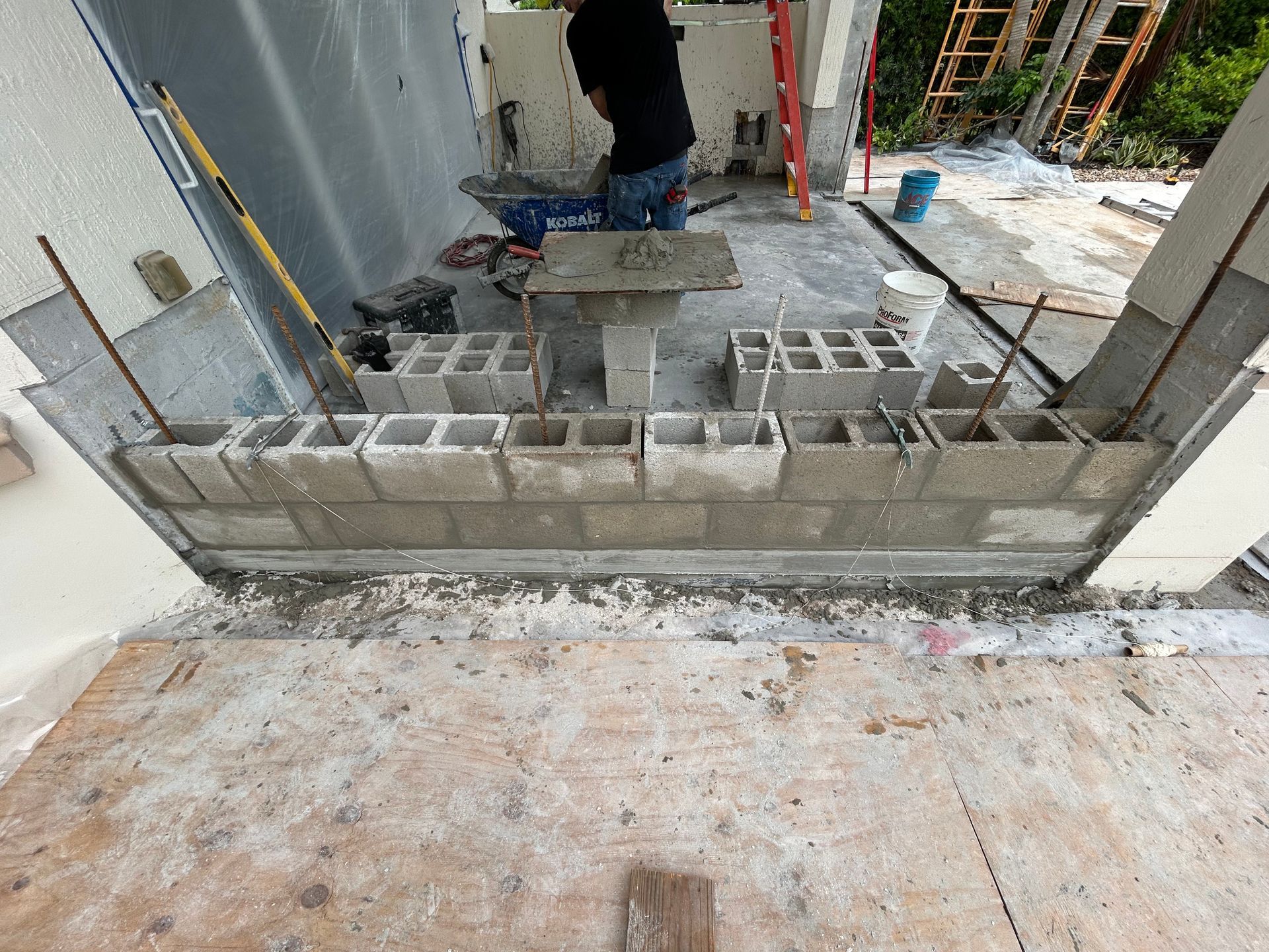 Construction worker laying cinder blocks, building a wall on a concrete structure, outdoors, overcast lighting.