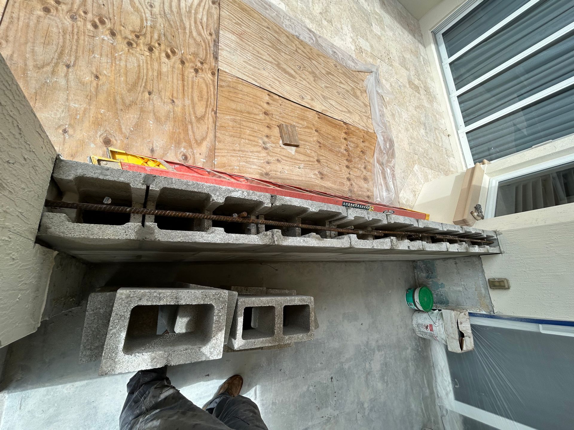 Construction site with concrete blocks, rebar, and wood paneling on a wall.