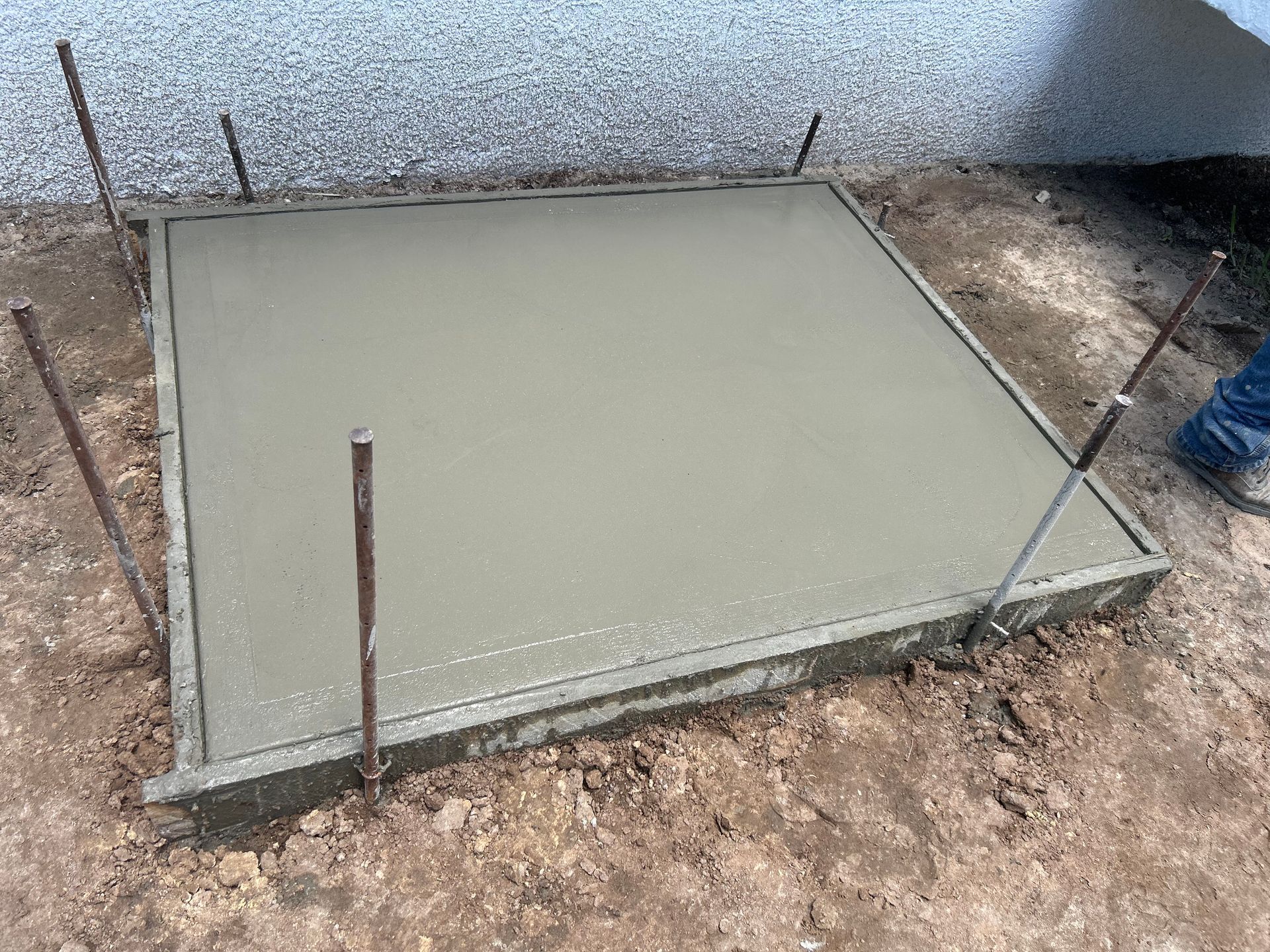 Fresh concrete poured into a square wooden frame, with rebar stakes, ready to set outside.