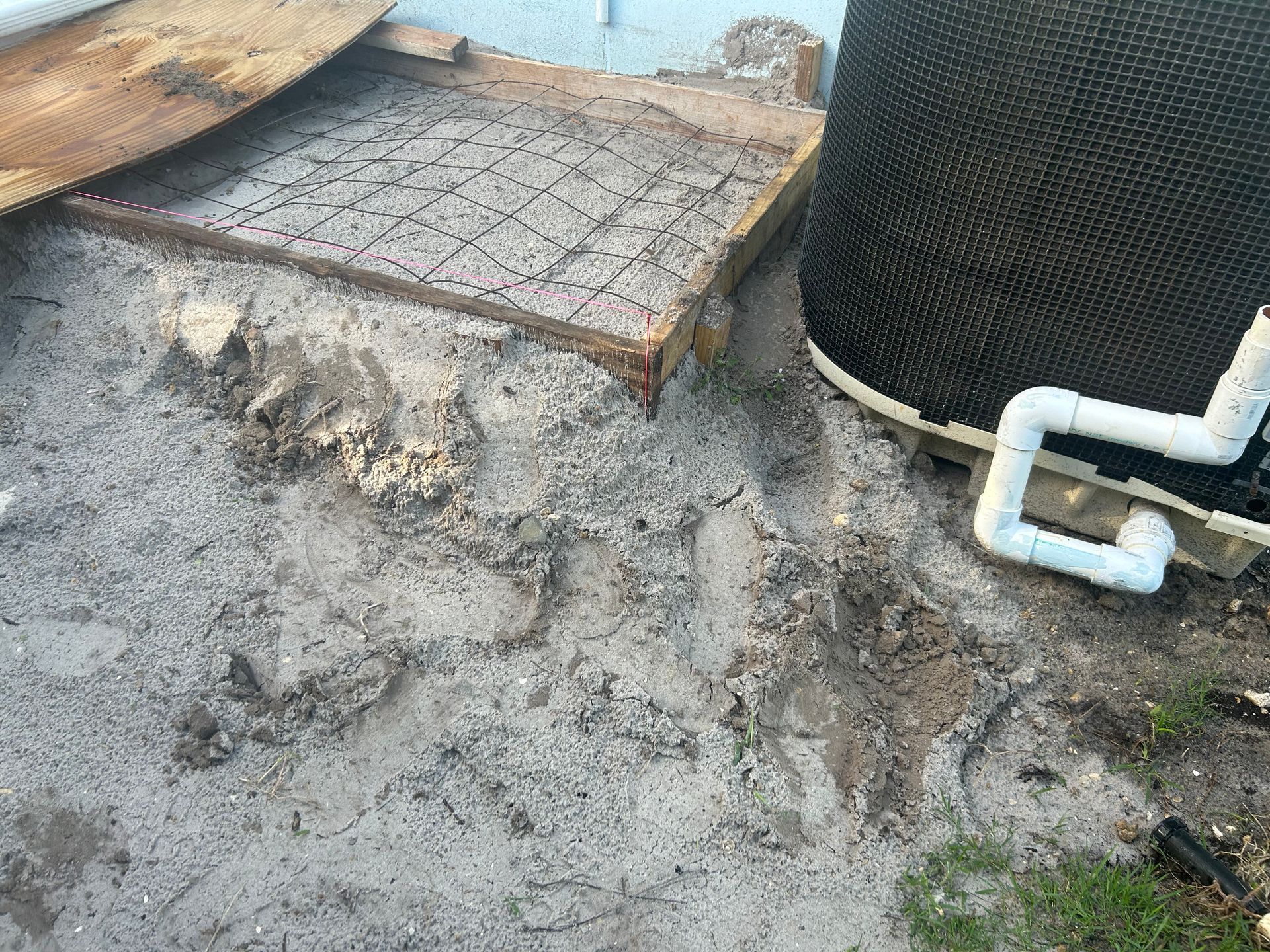 Sand ground with a wooden frame and a black textured structure next to white pipes.