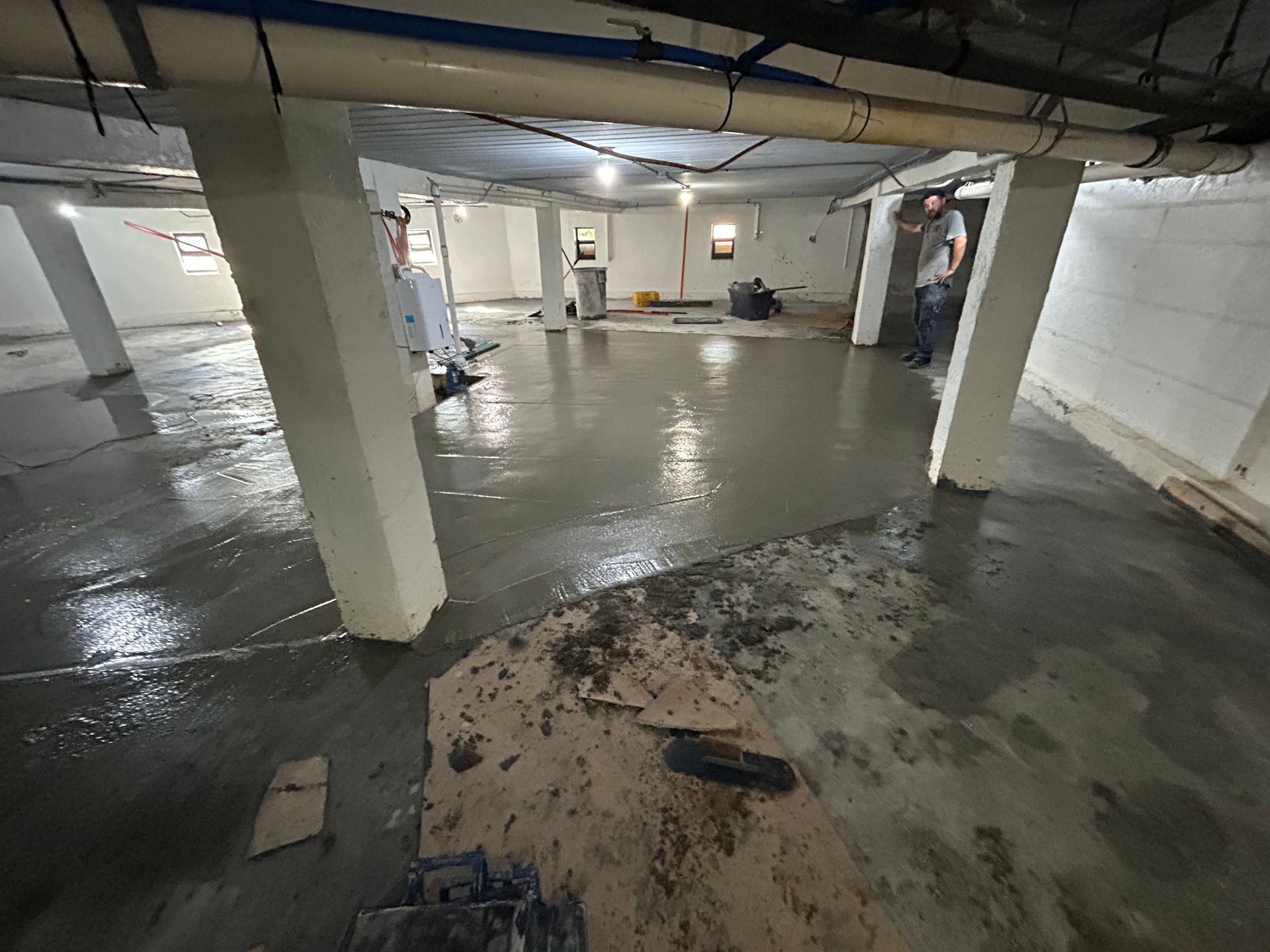 Basement with wet cement floor, support columns, and workers.