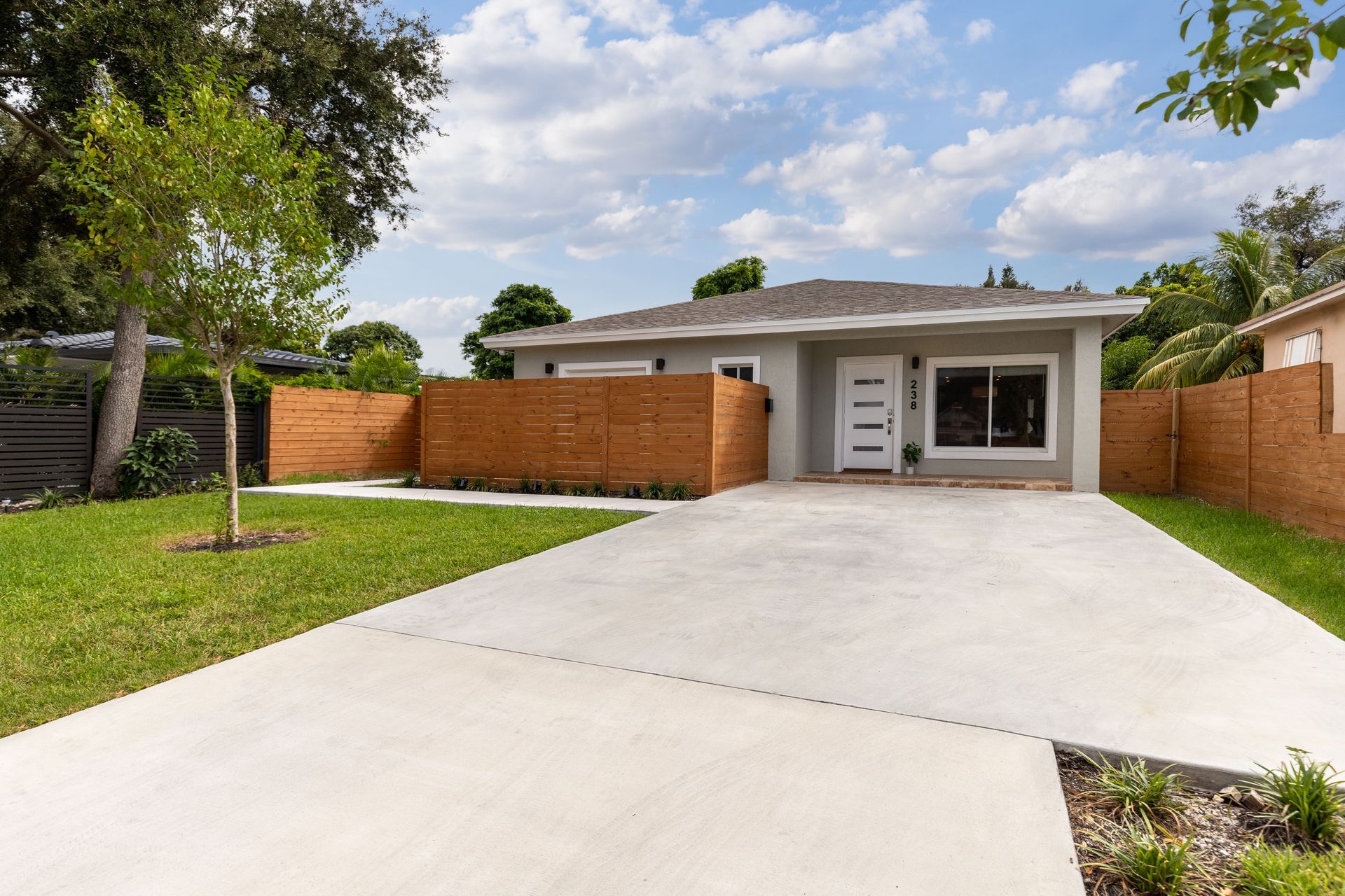 A concrete driveway leading to a house with a white fence