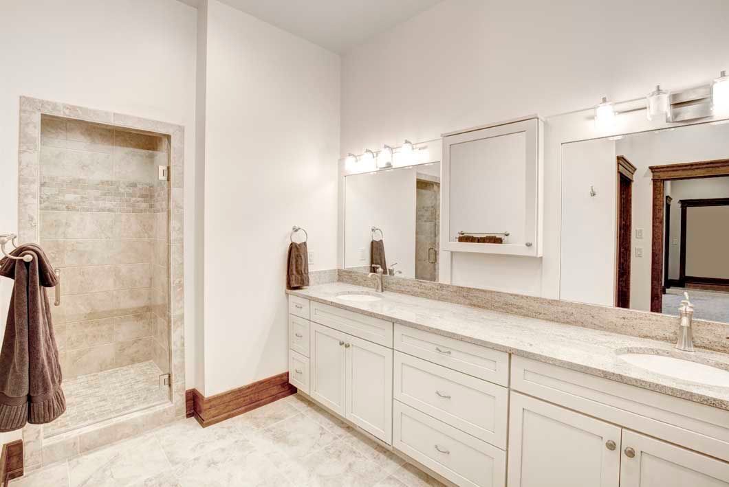 A bathroom with two sinks , two mirrors and a walk in shower.