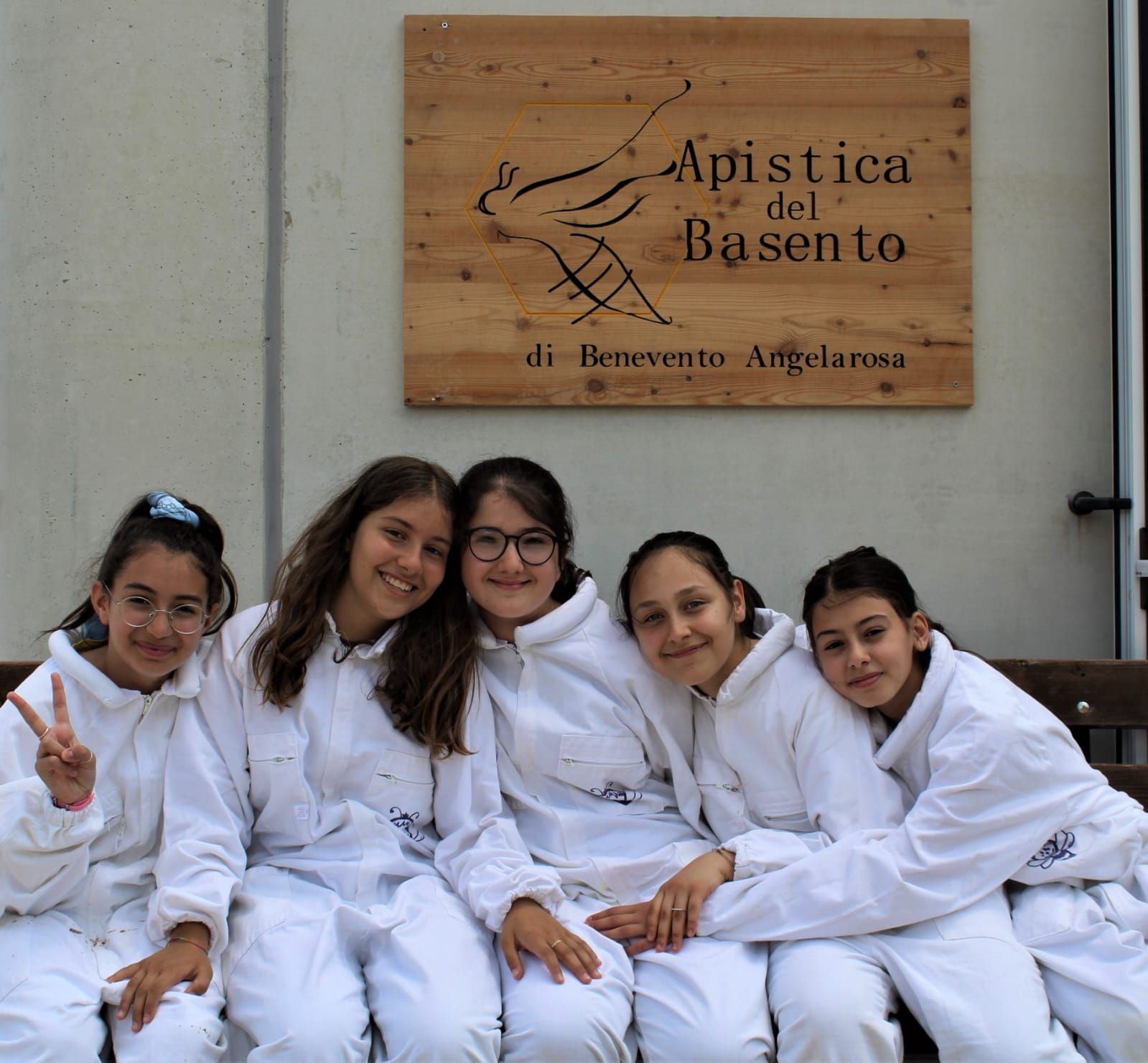 Un gruppo di ragazze è seduto su una panchina sotto un cartello che dice apistica del basento