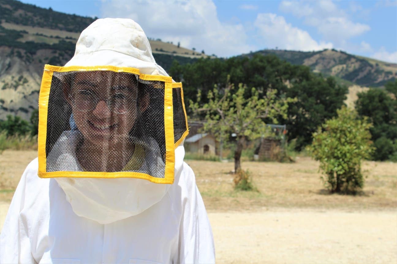 Un uomo che indossa una maschera da apicoltore è in piedi in un campo.