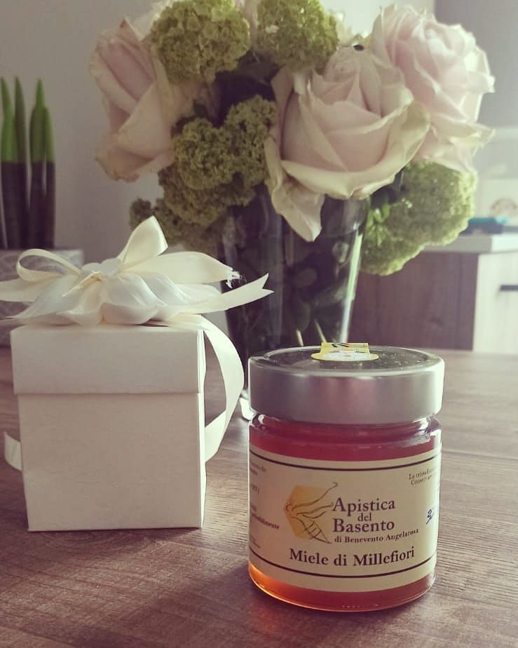 Un barattolo di miele è appoggiato su un tavolo accanto a un vaso di fiori