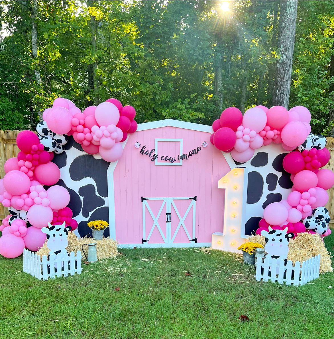 Pink barn-themed first birthday party decorations with balloon arches, cow spots, and a 