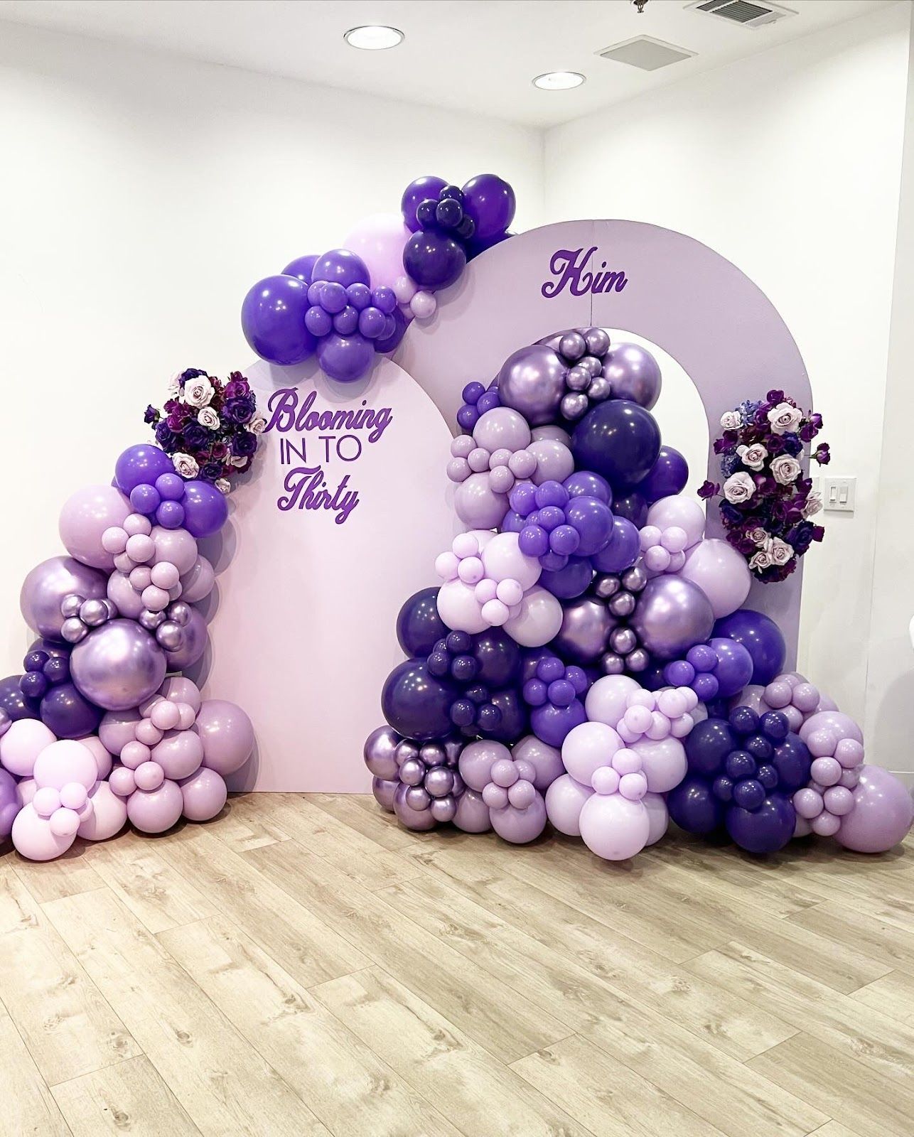 Purple balloon arch with floral accents; a light purple backdrop with text 